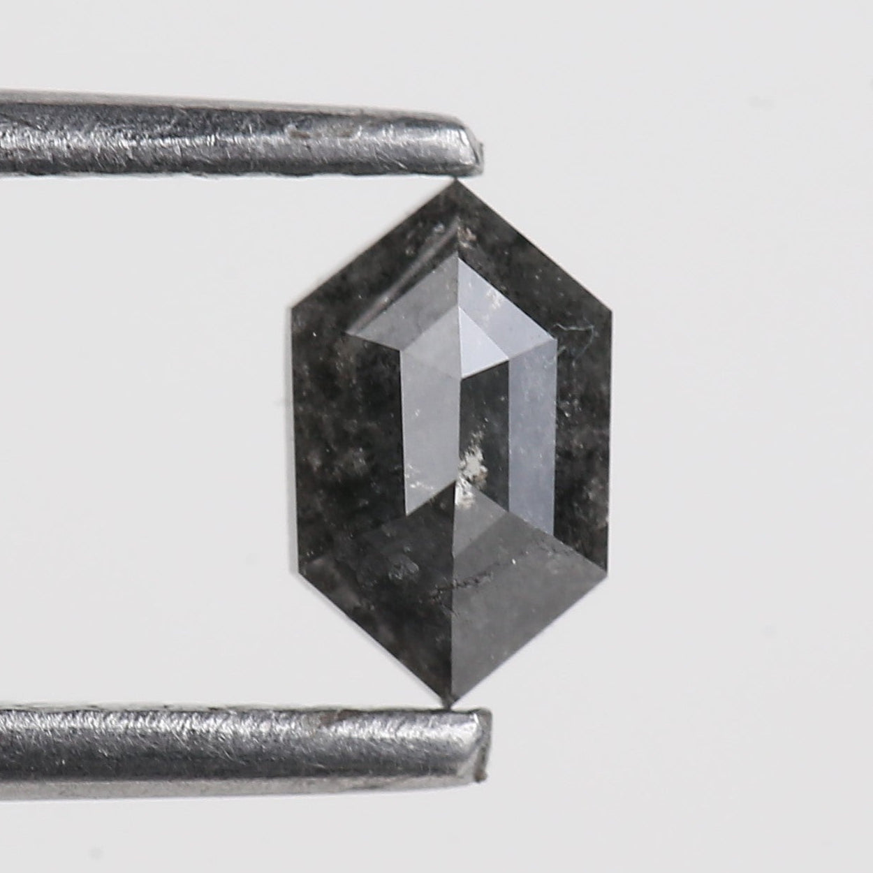 Hexagonal black diamond held by tweezers on a light gray background