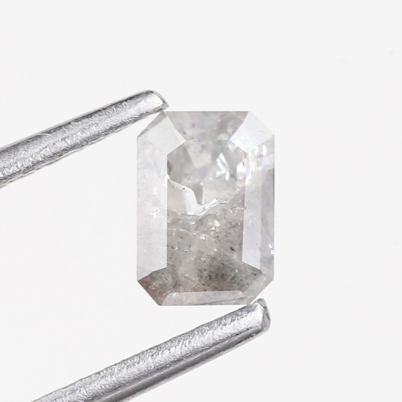 Rectangular diamond held by tweezers on a white background