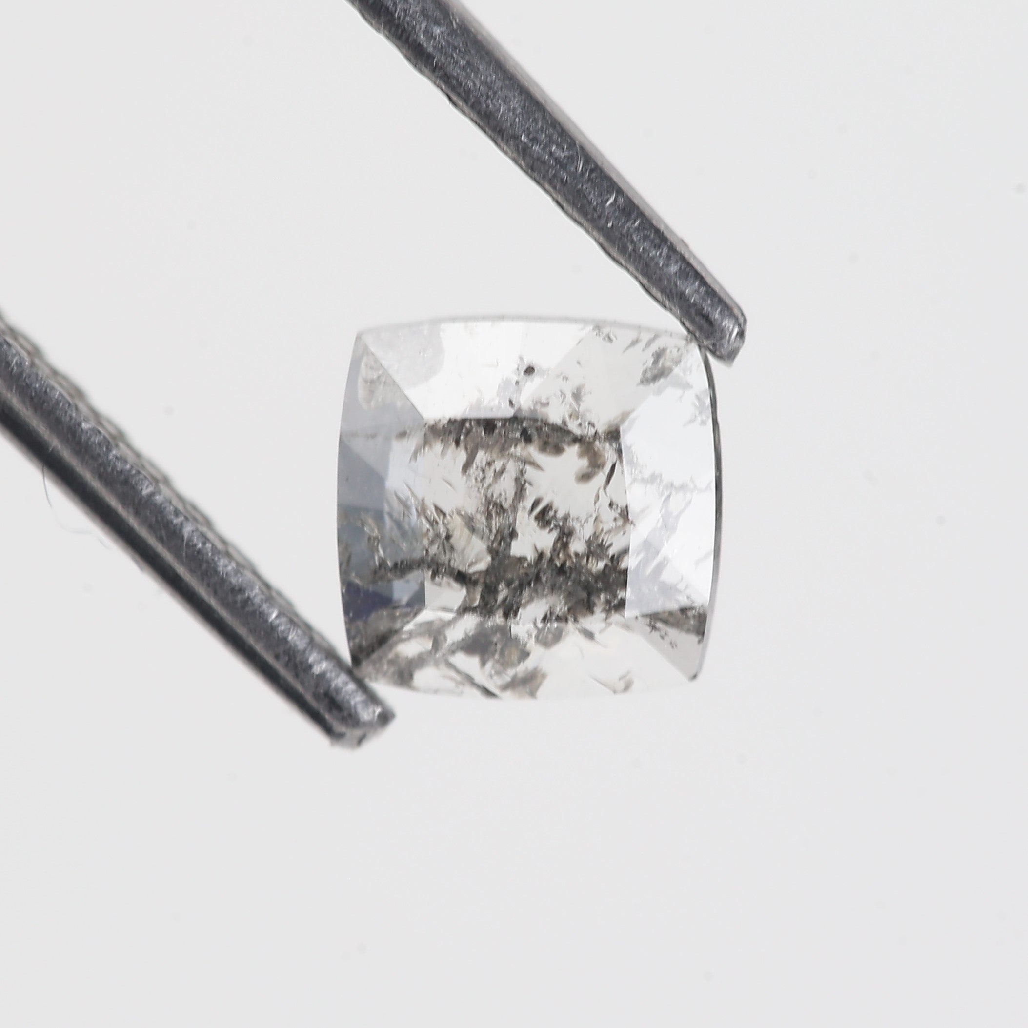 Square-cut diamond held by tweezers on a light gray background