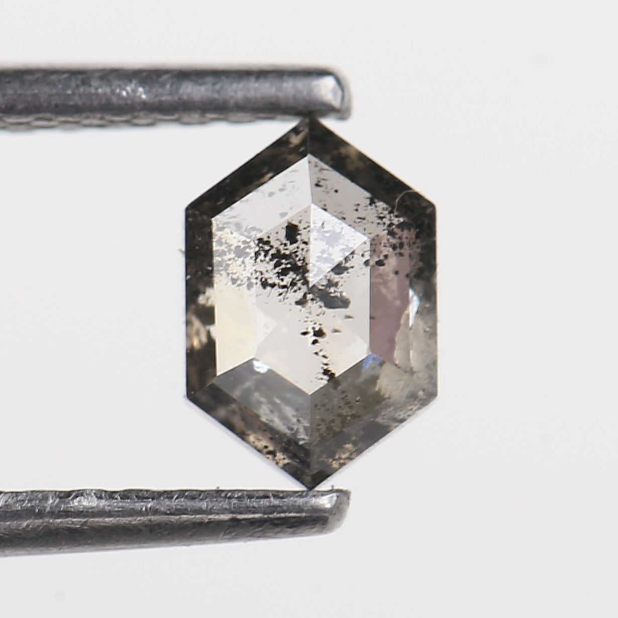 Hexagonal diamond held between tweezers on a light gray background