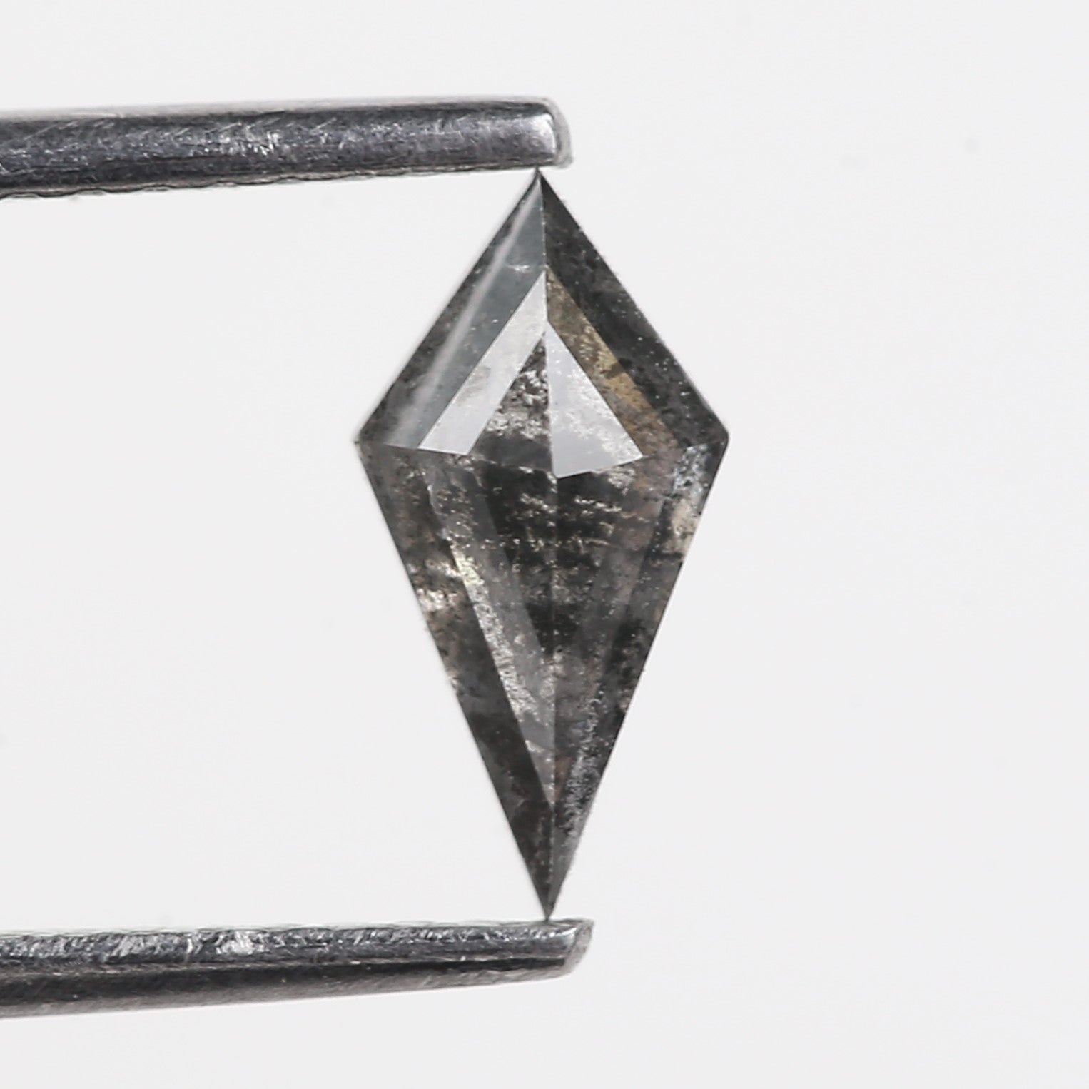 Faceted gemstone held by tweezers on a light gray background