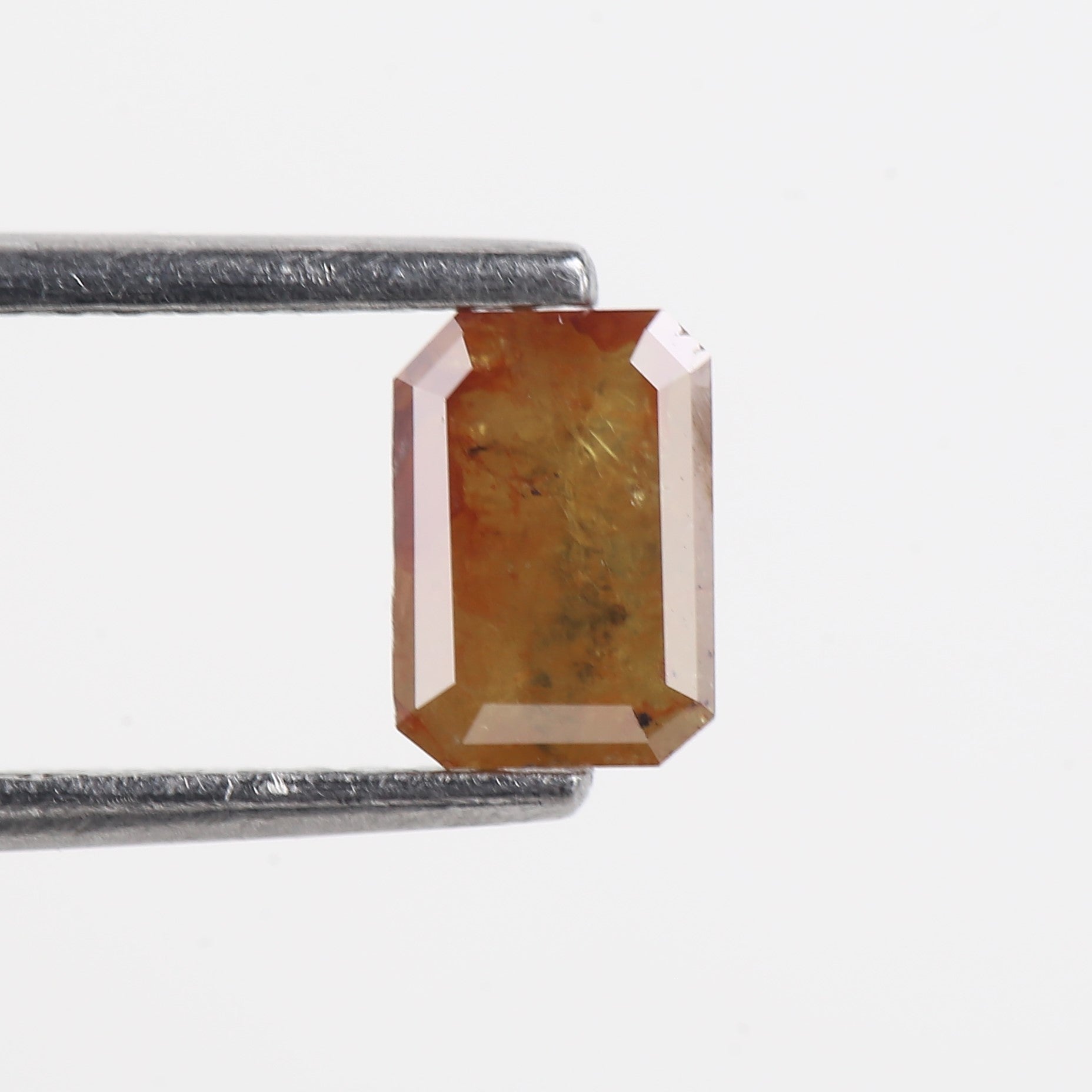 Rectangular brown gemstone held by tweezers on a white background