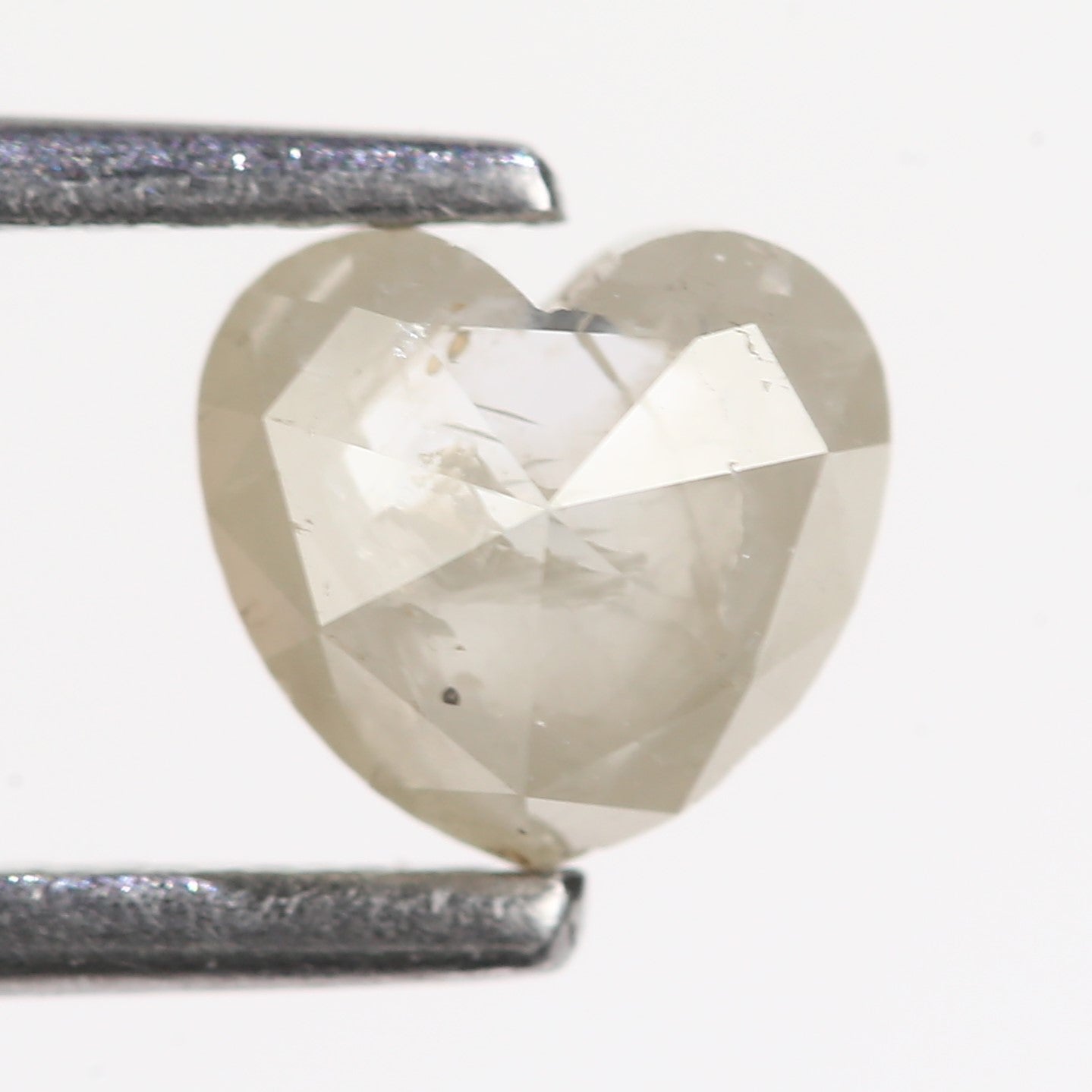 Heart-shaped diamond held between two tweezers on a white background