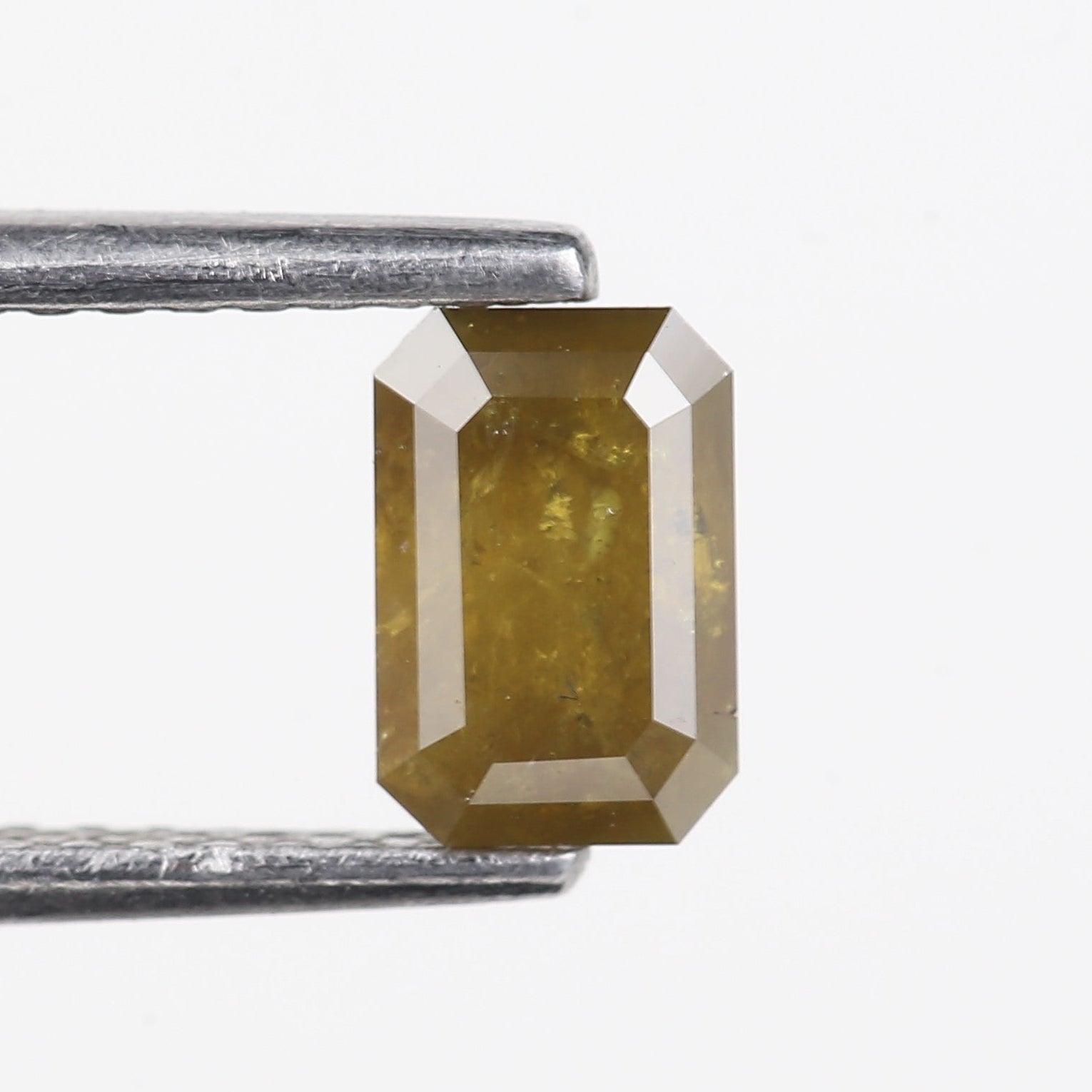 Faceted gemstone held between tweezers on a white background