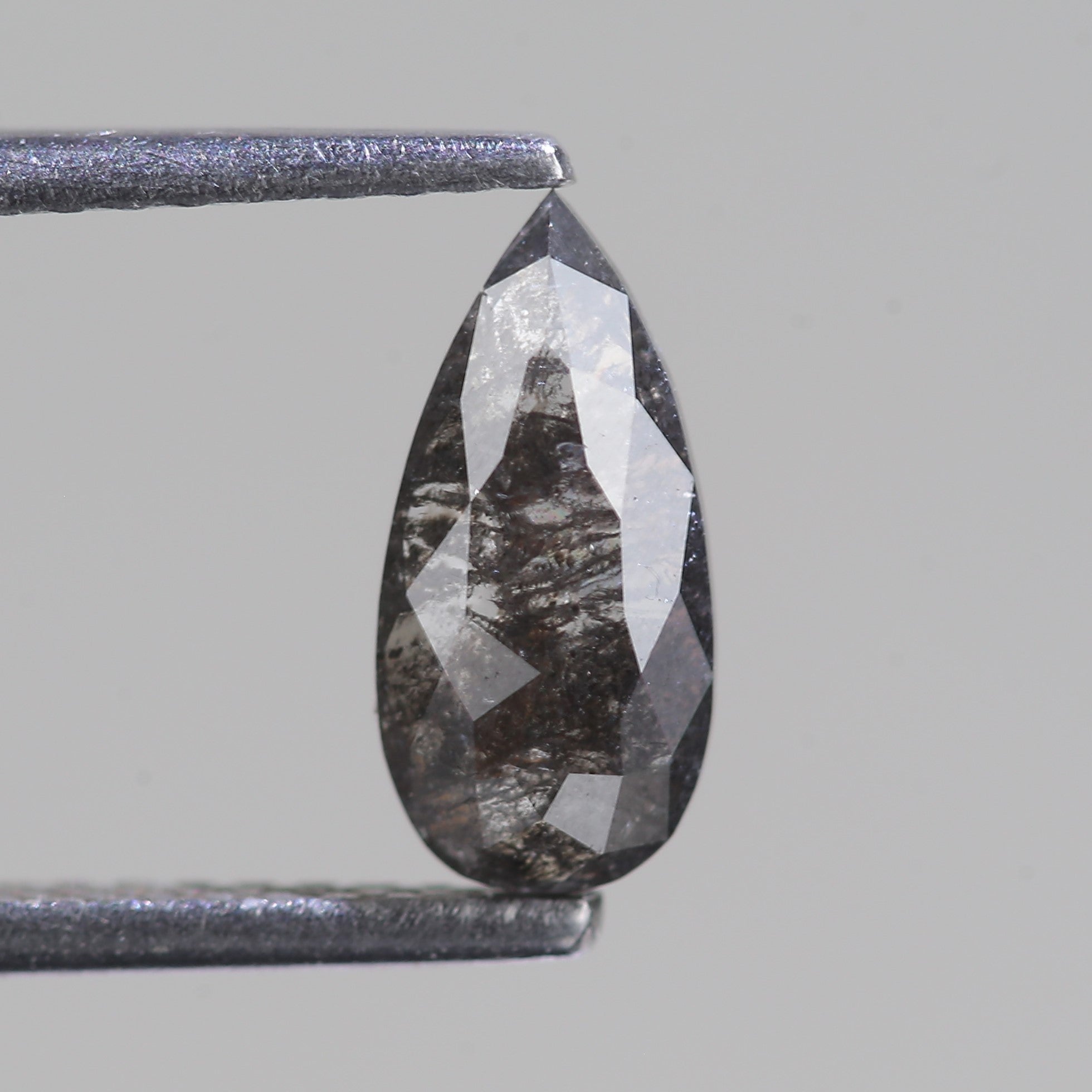 Teardrop-shaped diamond held between tweezers on a gray background