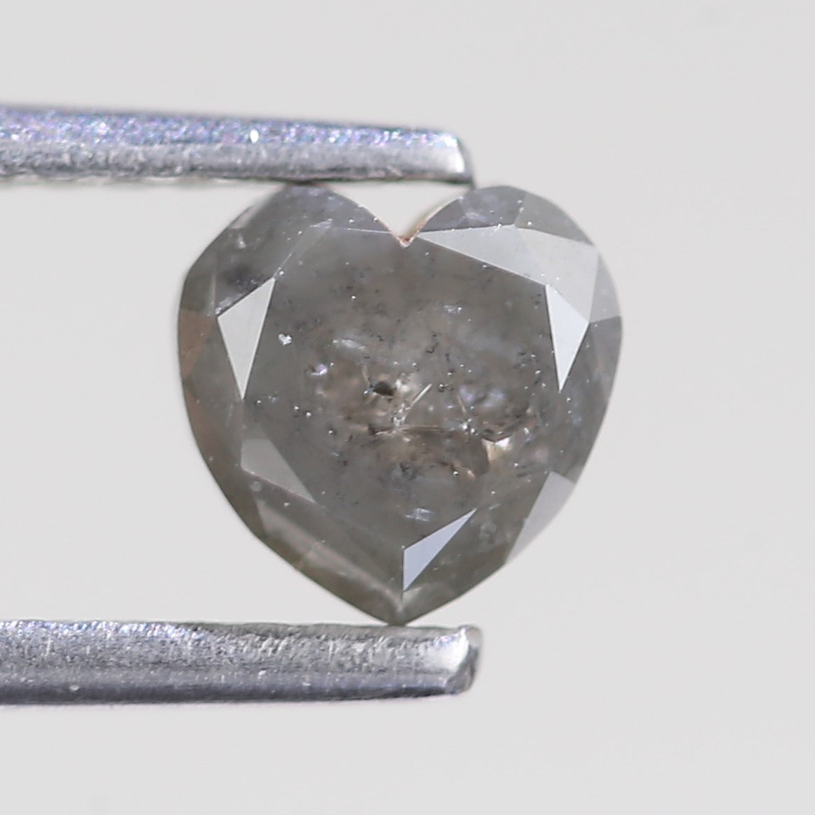 Heart-shaped diamond with a metal gage for scale on a light gray background