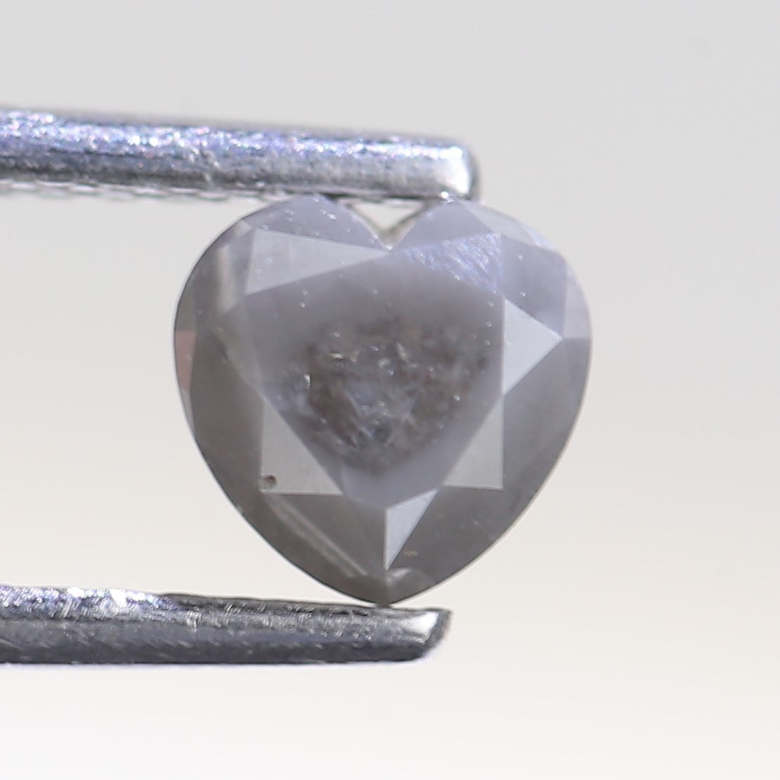 Heart-shaped grayish-blue diamond held by tweezers on a light gray background