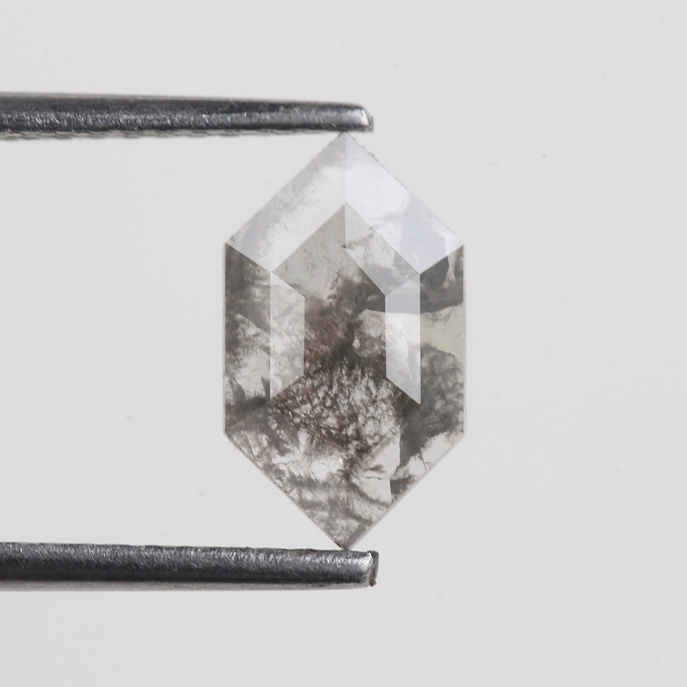 Hexagonal crystal held by tweezers on a light gray background