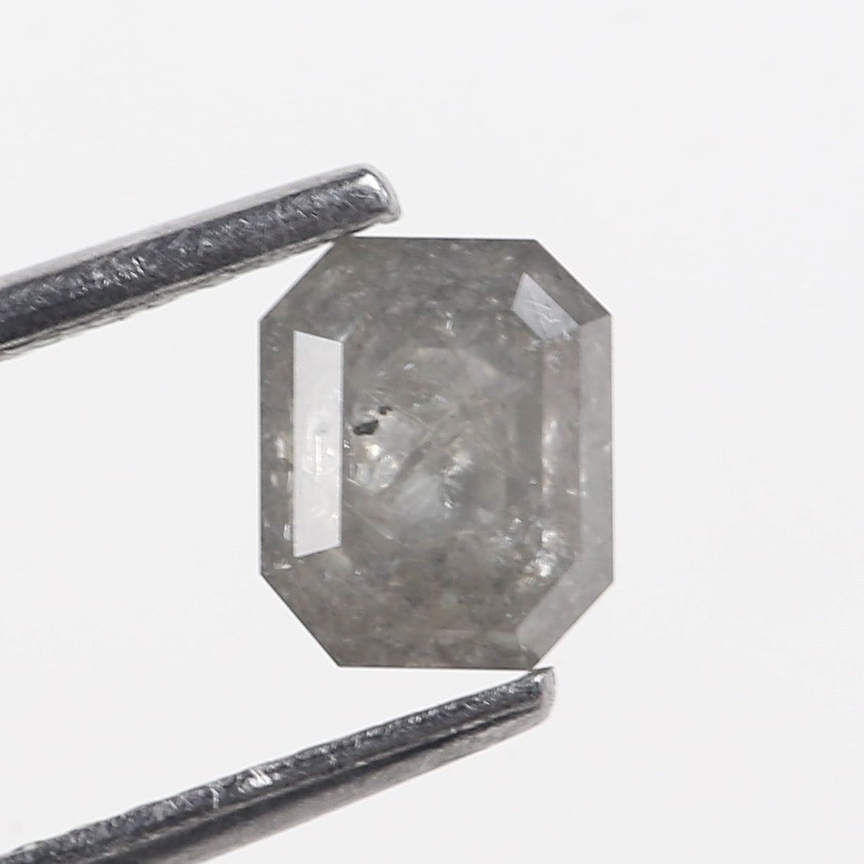 Emerald diamond held between tweezers on a white background