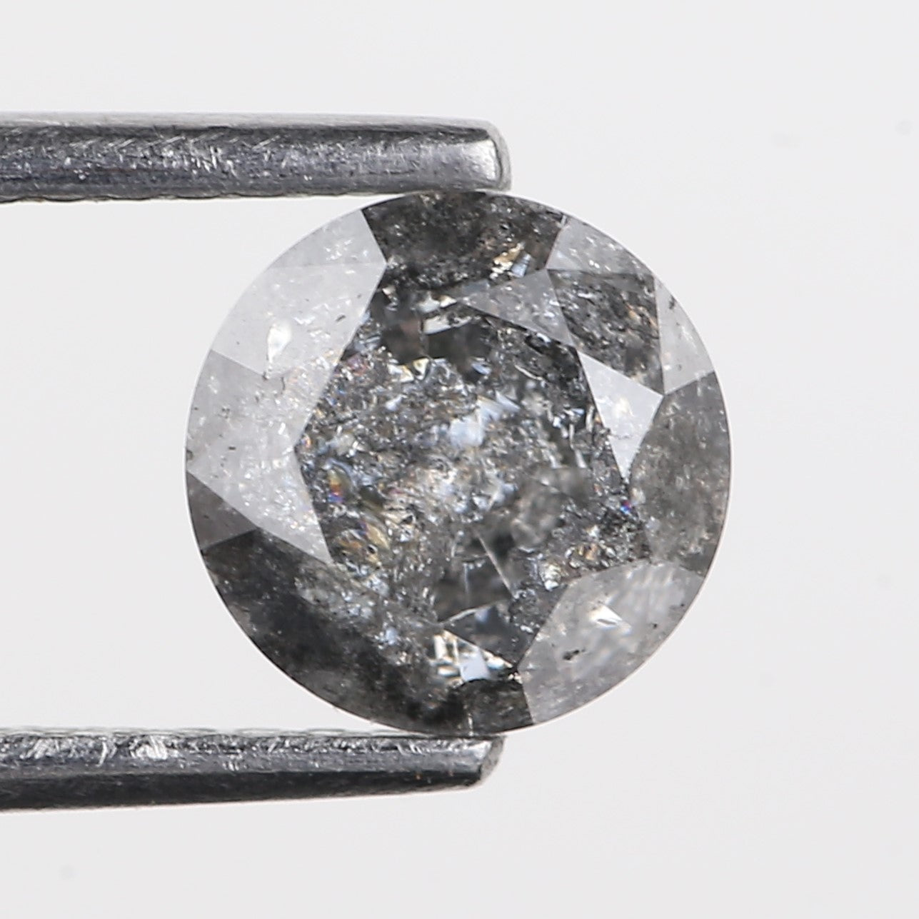 Round diamond held between tweezers on a light gray background