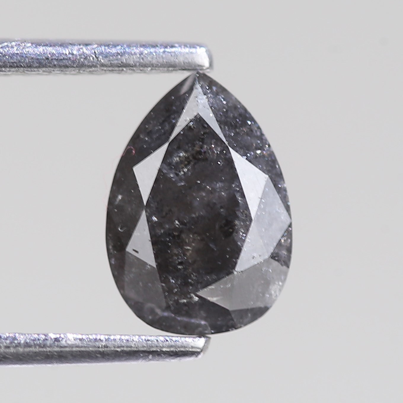 Teardrop-shaped diamond held between two silver prongs against a light gray background