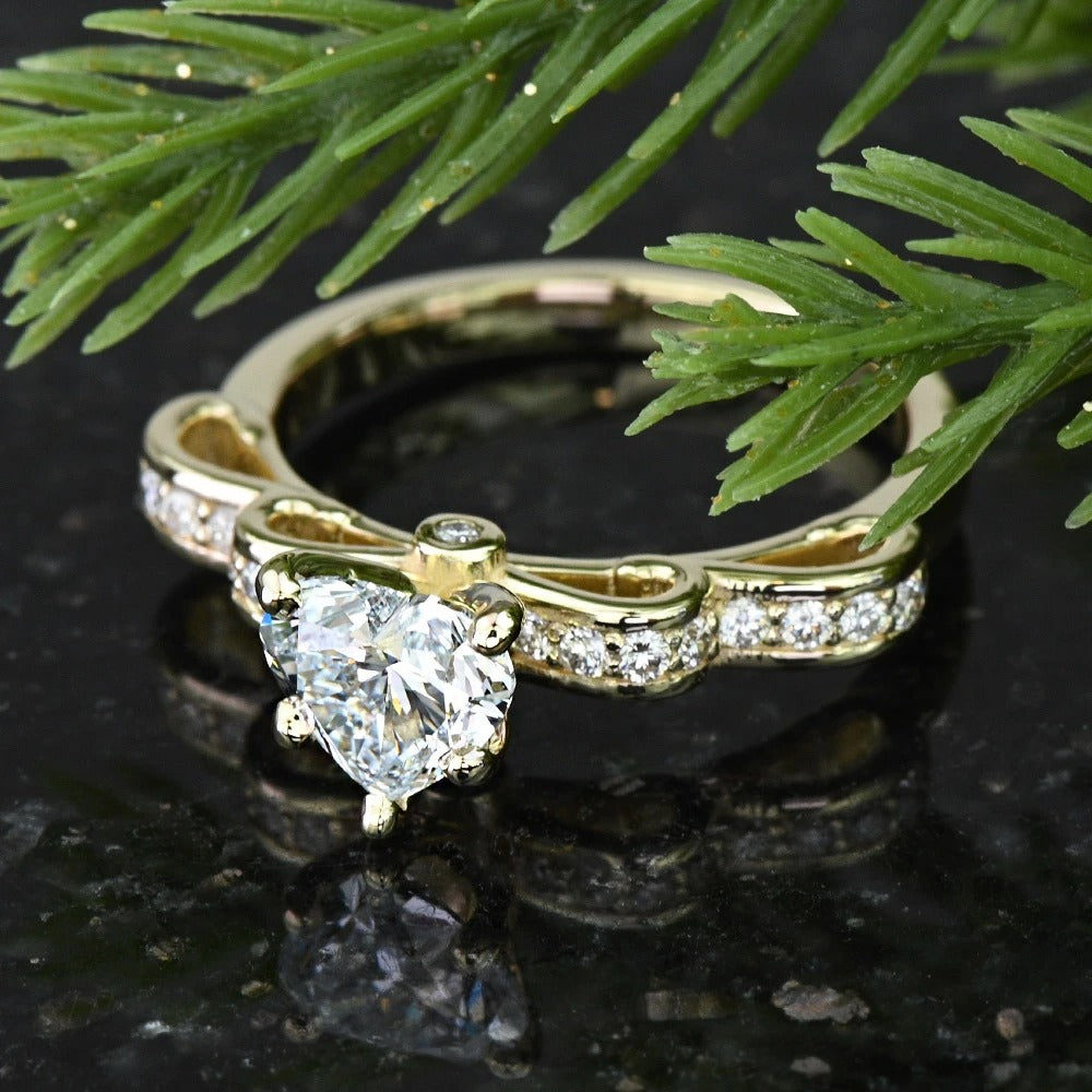 Gold ring with heart-shaped diamond on a dark surface with green leaves