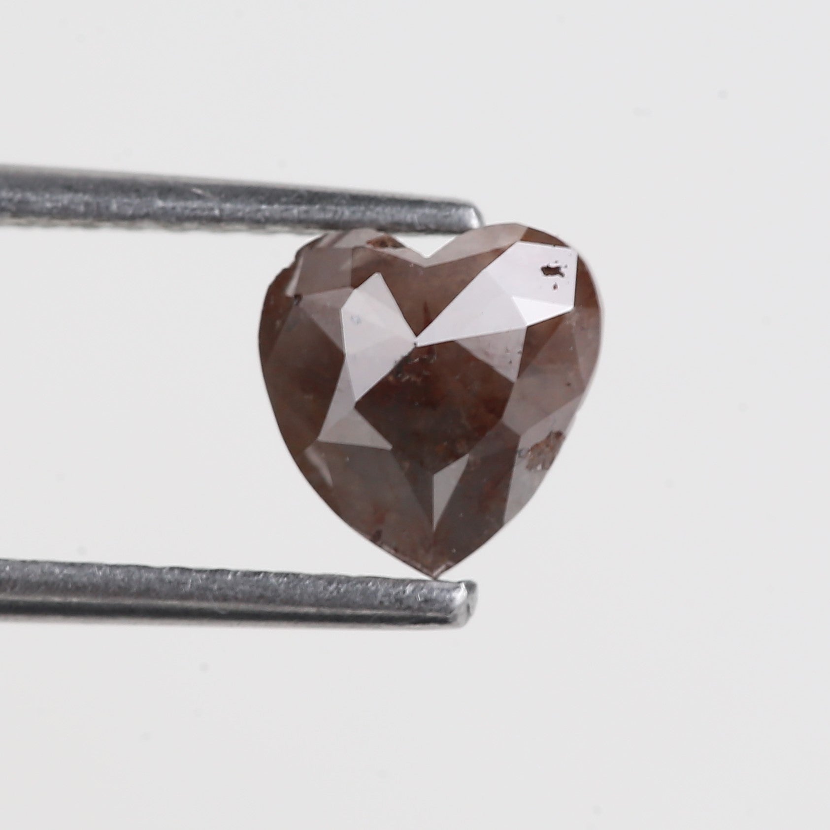 Heart-shaped red brown diamond held by tweezers on a light gray background