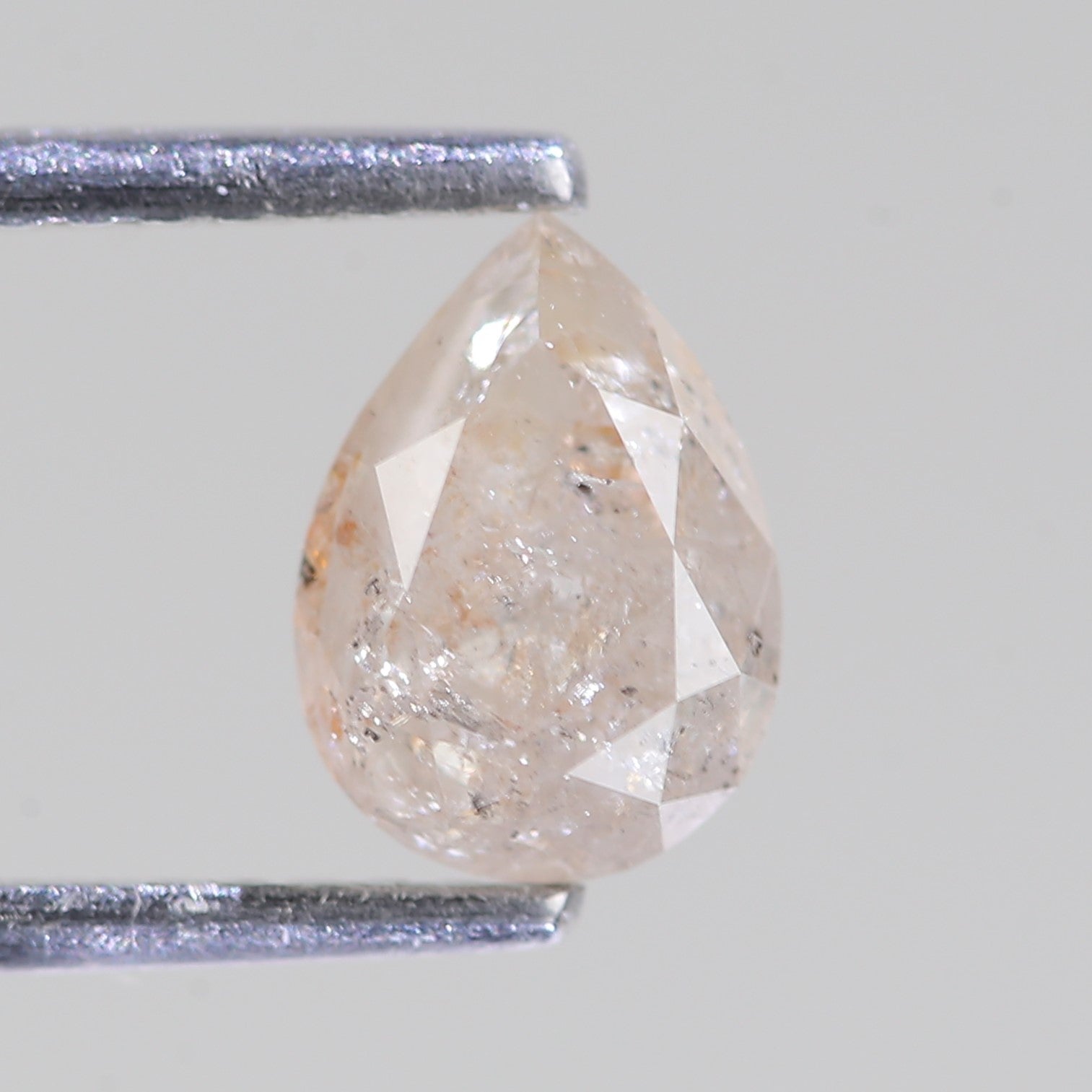 Pear-shaped diamond held between two metal prongs on a light gray background