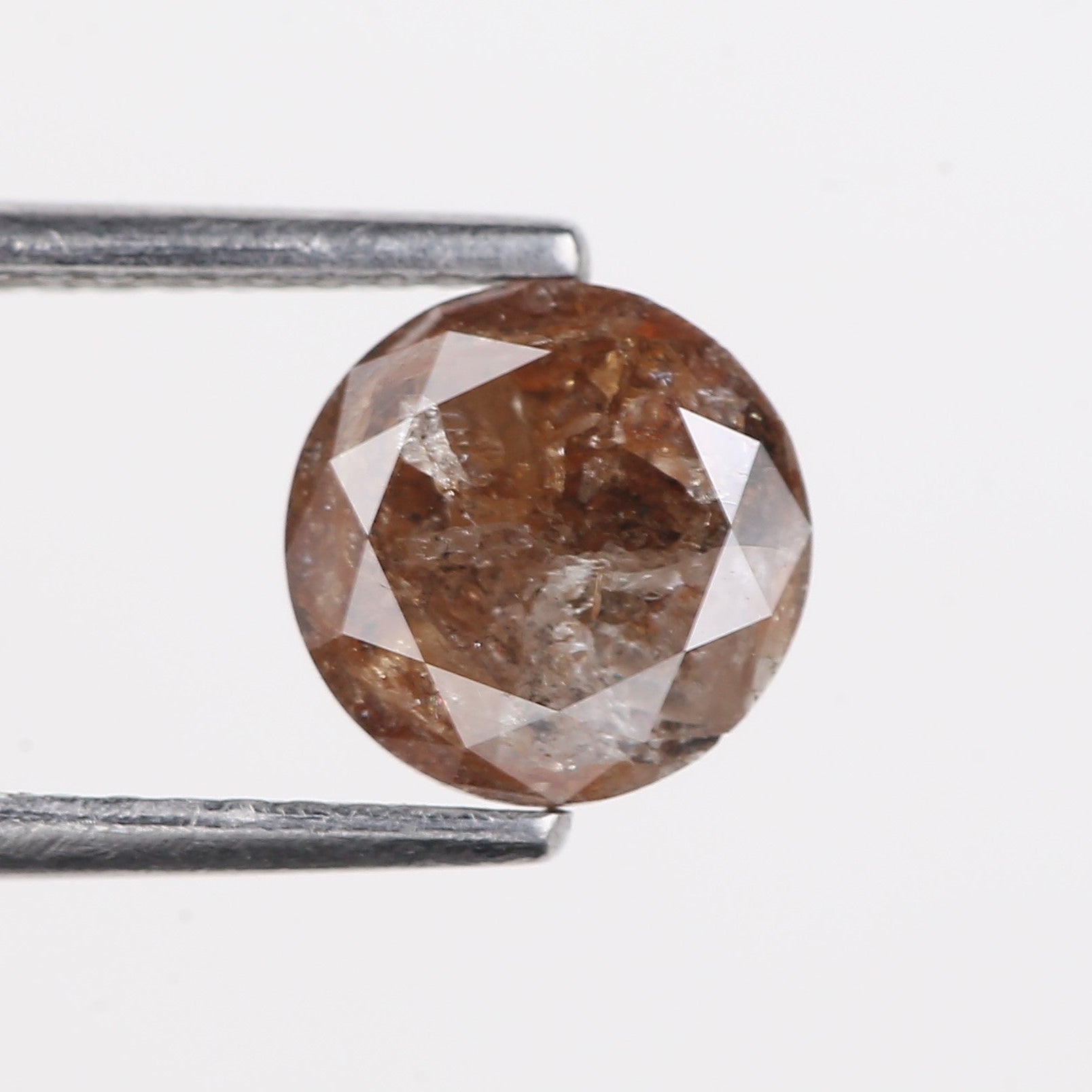 Brown diamond held by tweezers on a light gray background