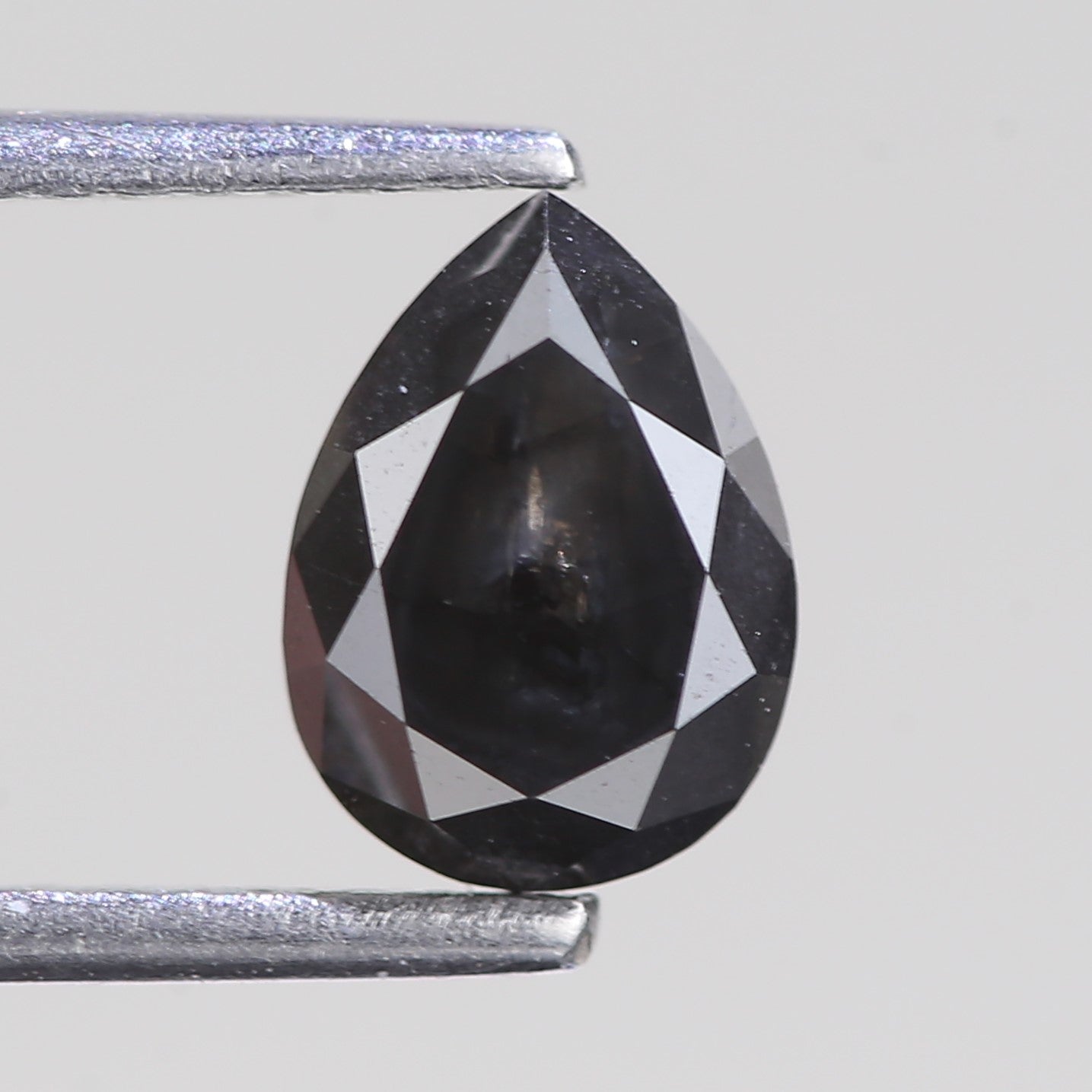 Teardrop-shaped black diamond between two silver prongs on a light gray background