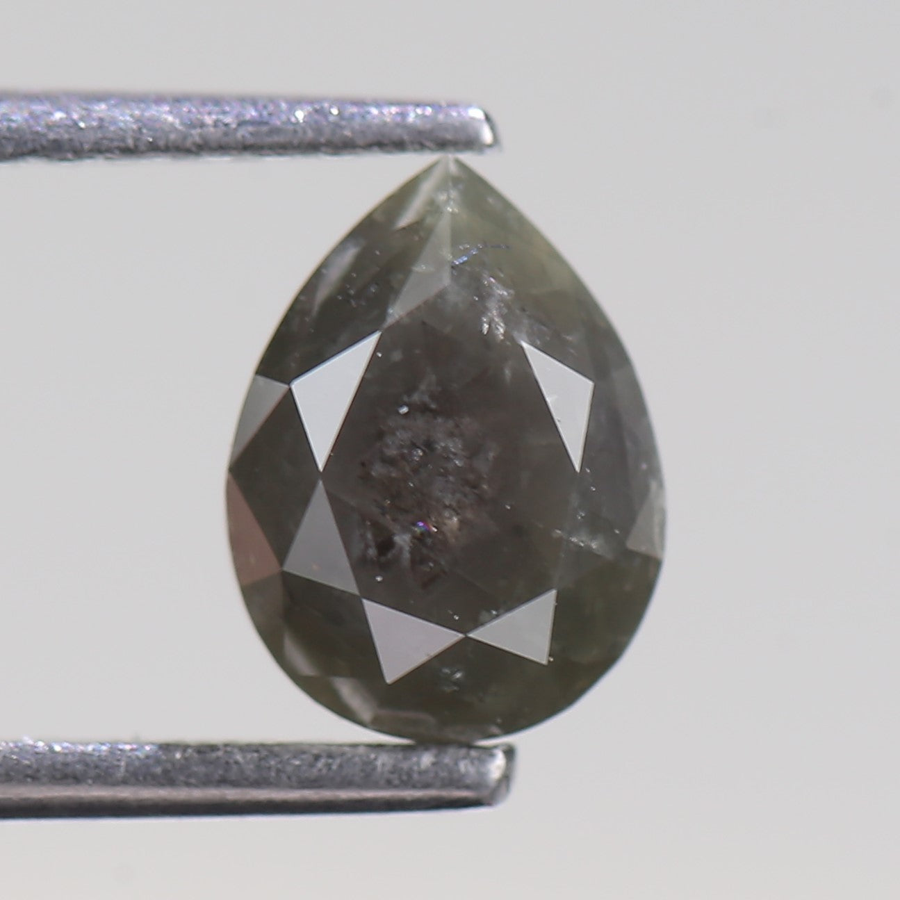 Teardrop-shaped diamond held between two metal prongs on a light gray background