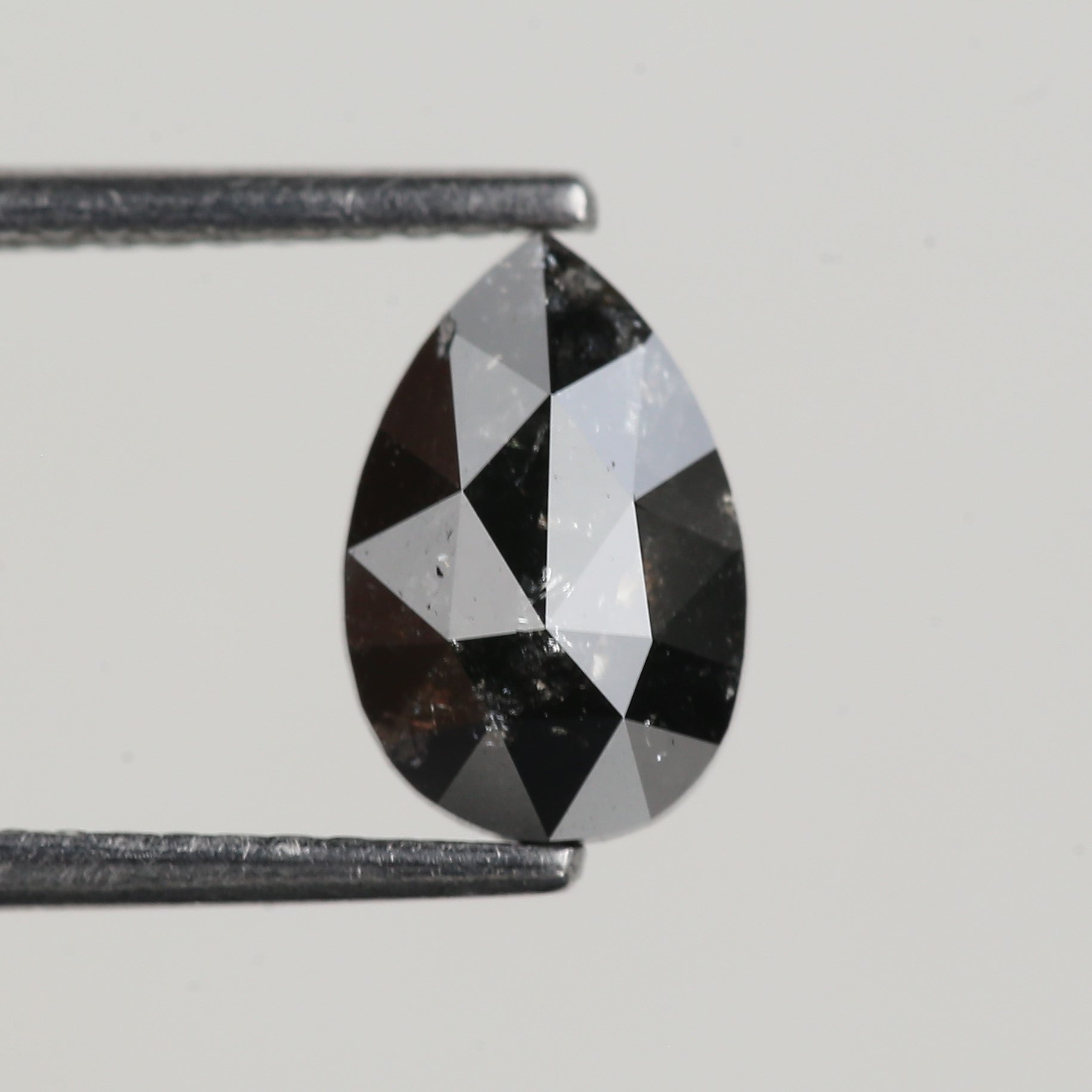 Teardrop-shaped black and white gemstone held by tweezers on a light gray background