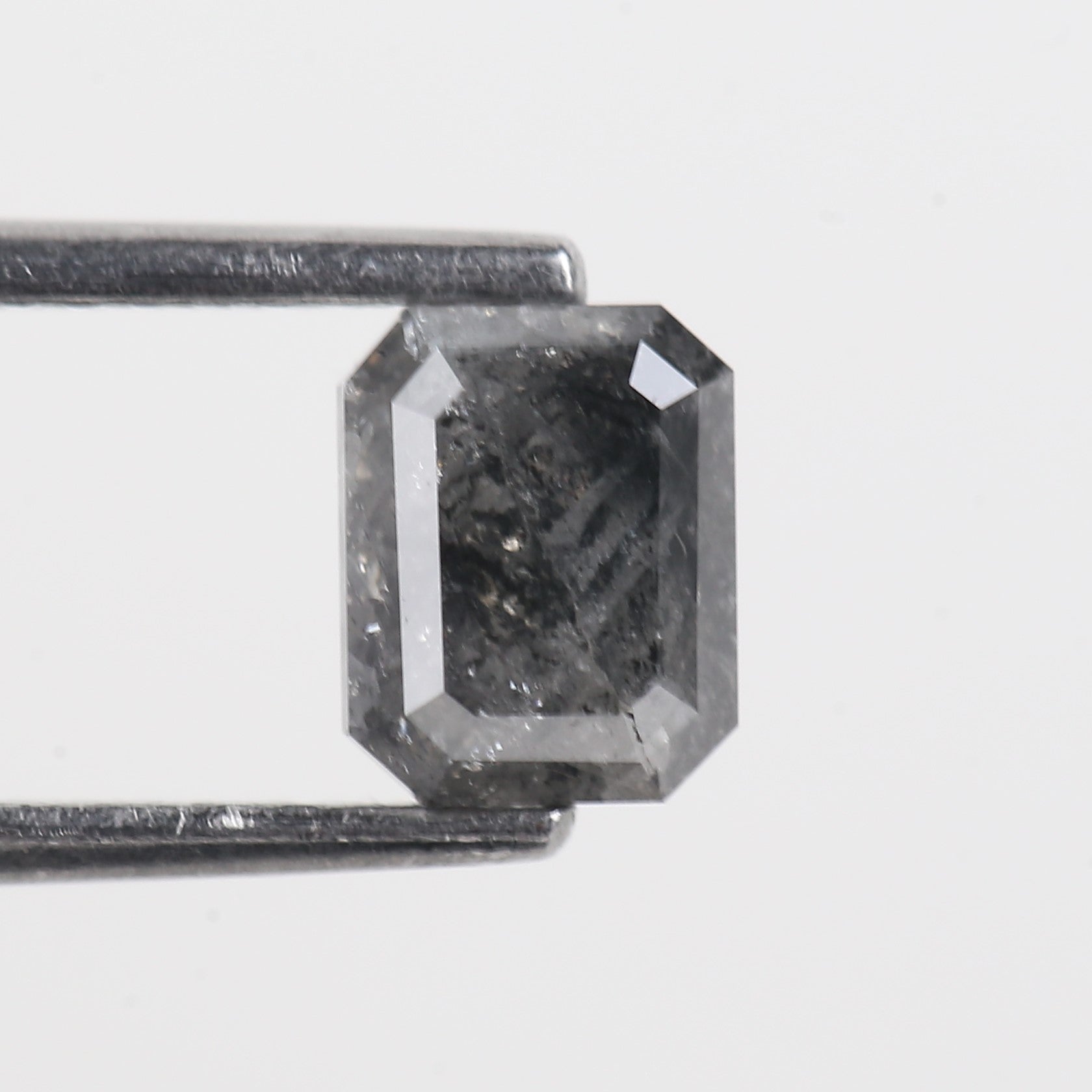 emerald grey black diamond held by tweezers on a light gray background