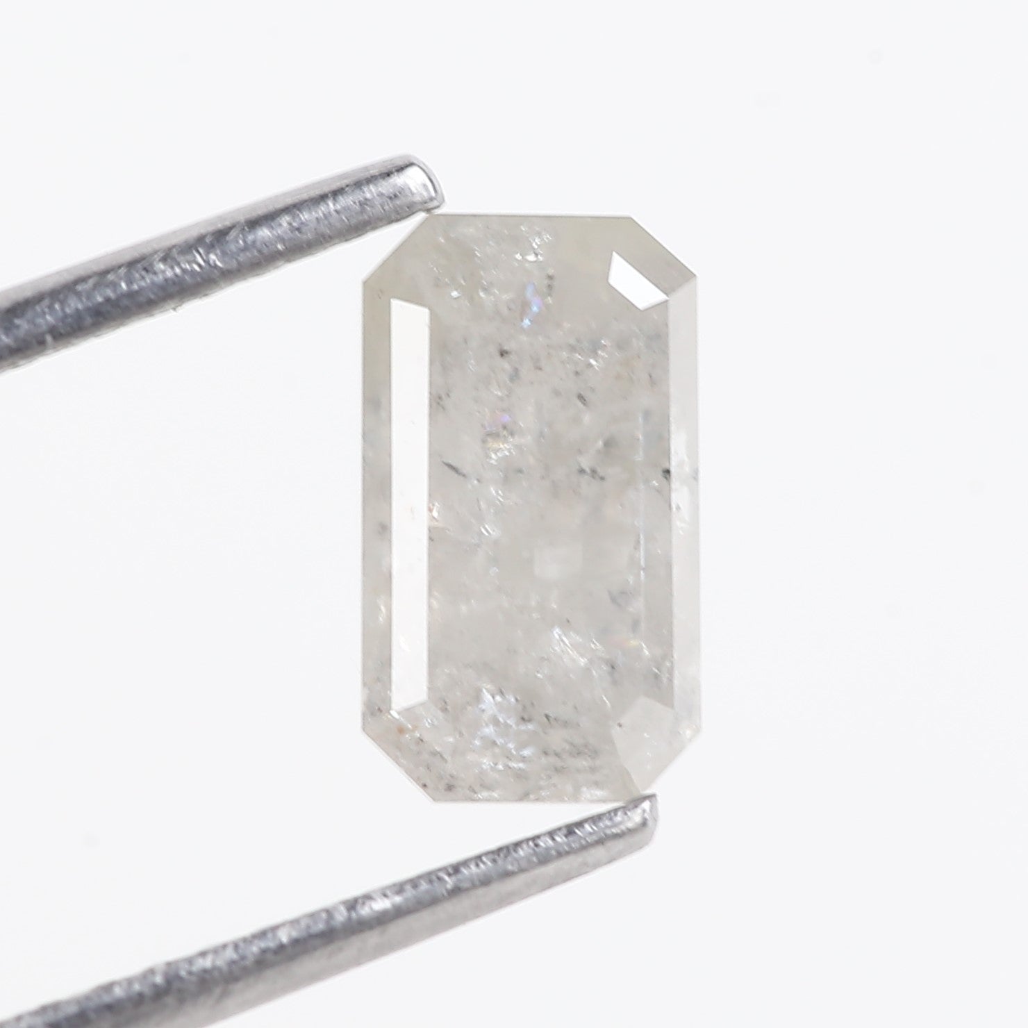 Rectangular diamond held by tweezers on a white background