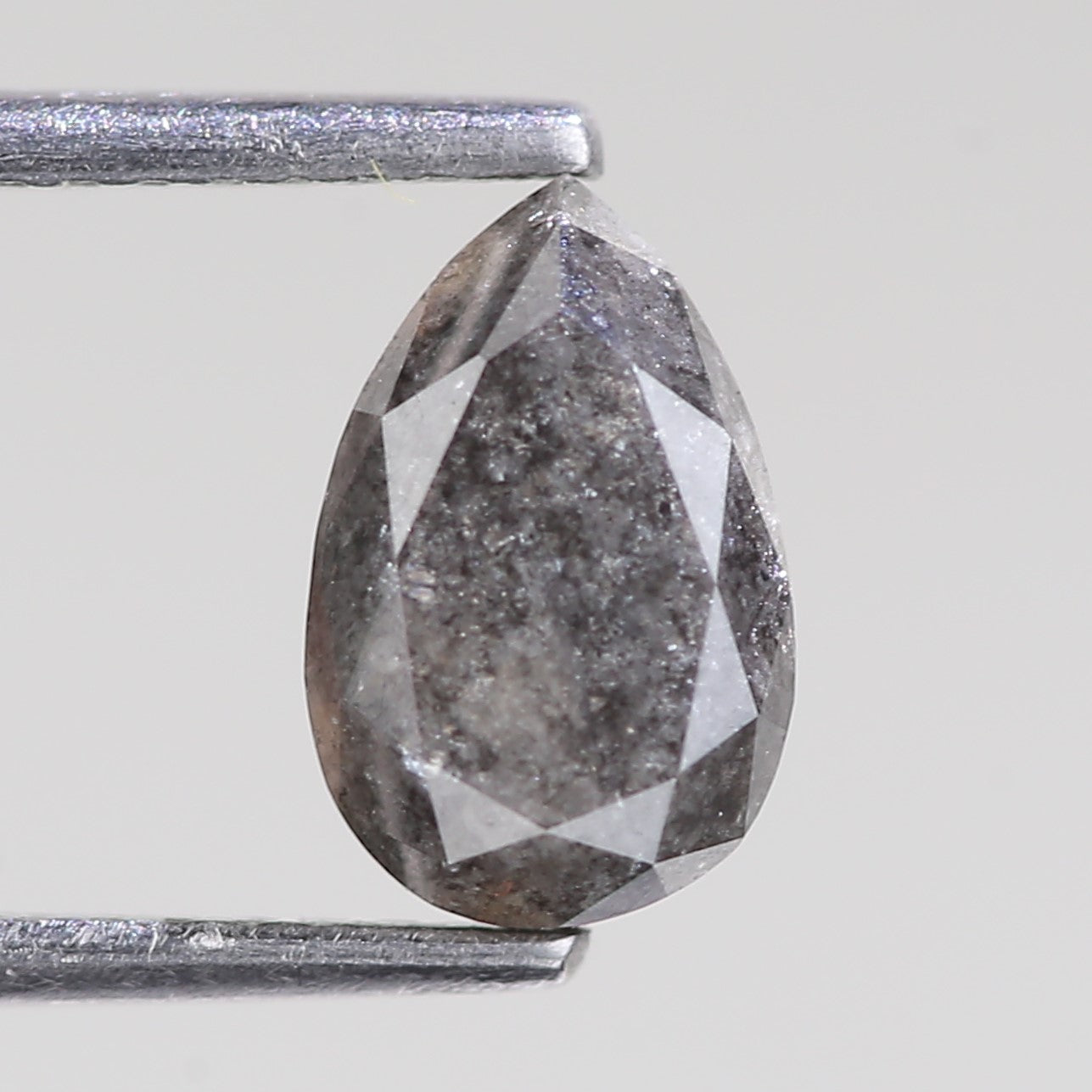 Teardrop-shaped diamond held between two metal prongs on a light gray background