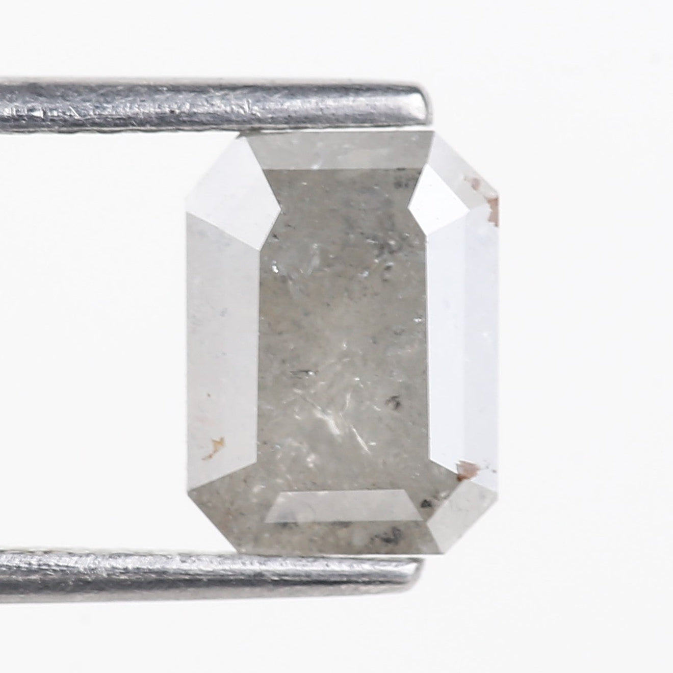 Rectangular diamond held by tweezers on a white background