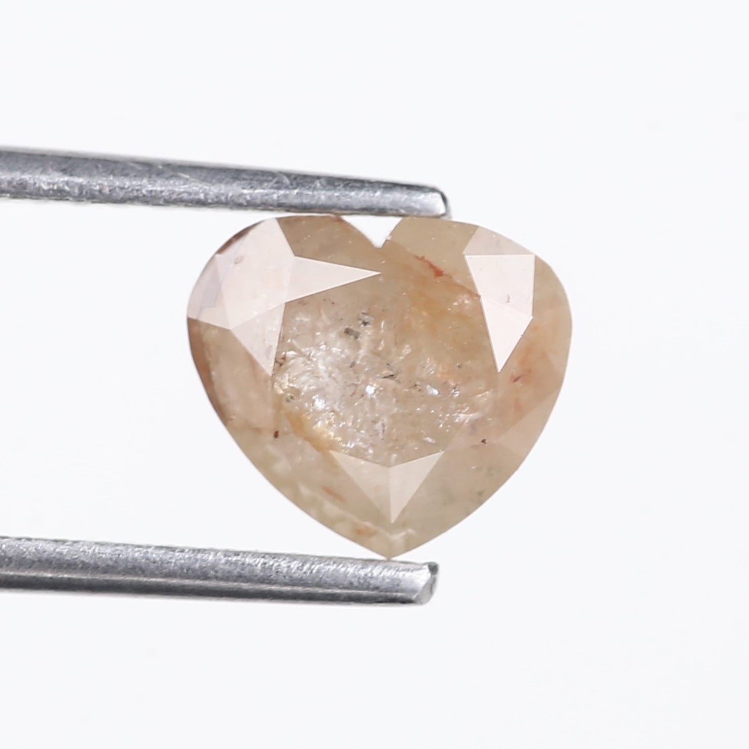 Heart-shaped diamond held by tweezers on a white background
