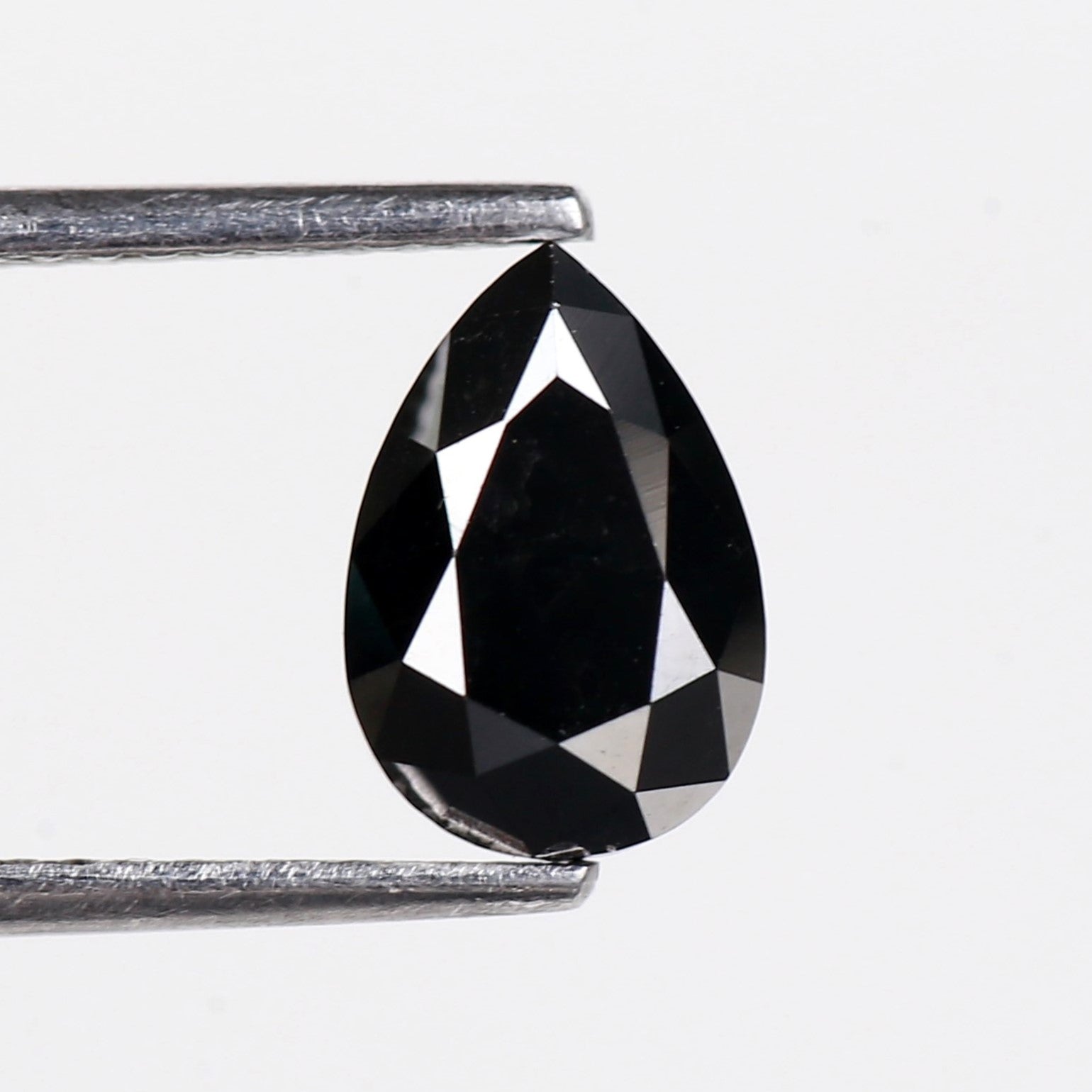 Teardrop-shaped black gemstone held by tweezers on a white background