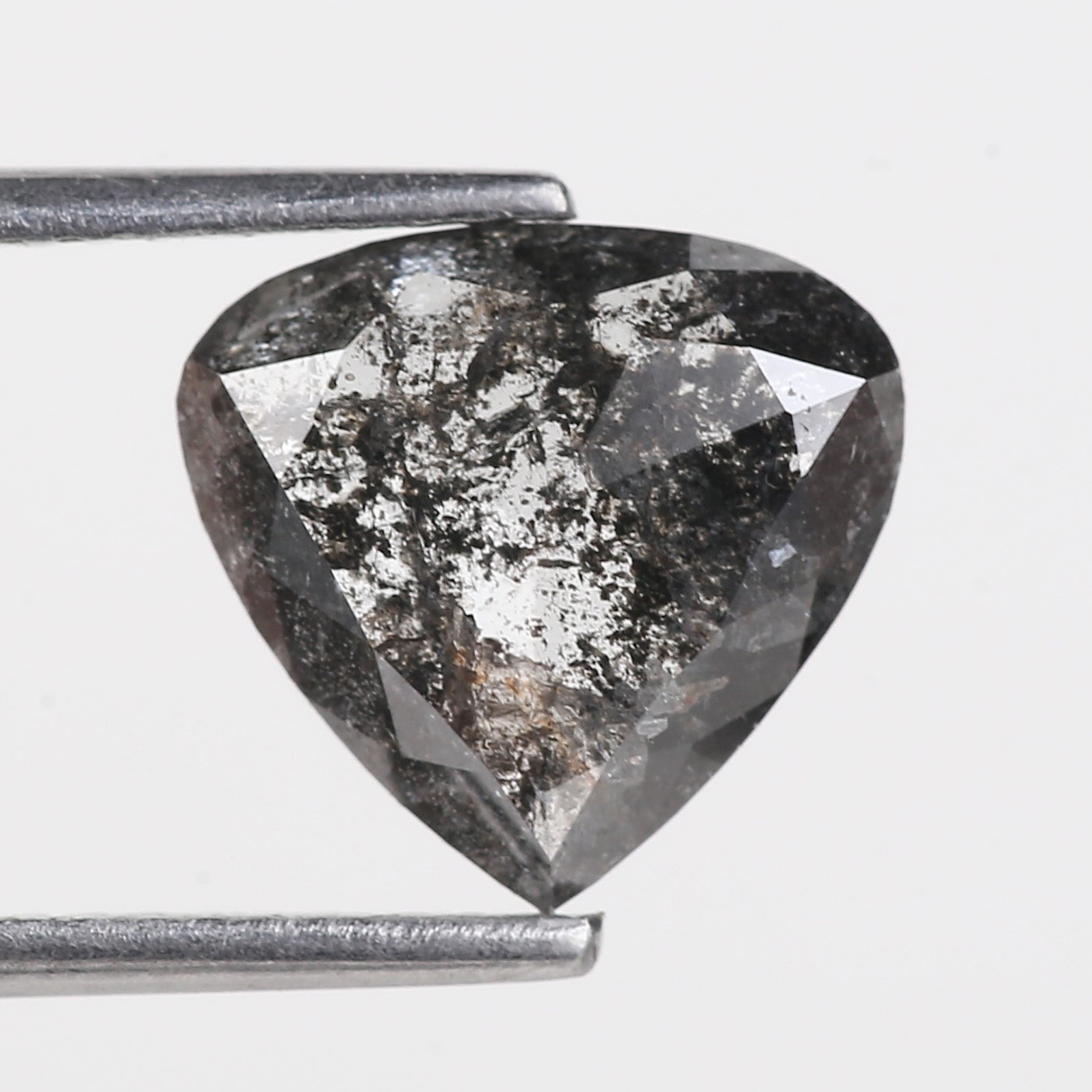 Trillion-shaped diamond with dark inclusions held by tweezers on a light gray background