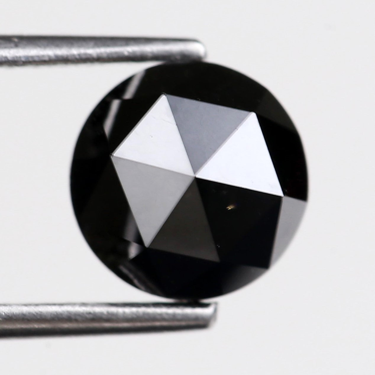 Faceted black black rose held between tweezers on a light gray background