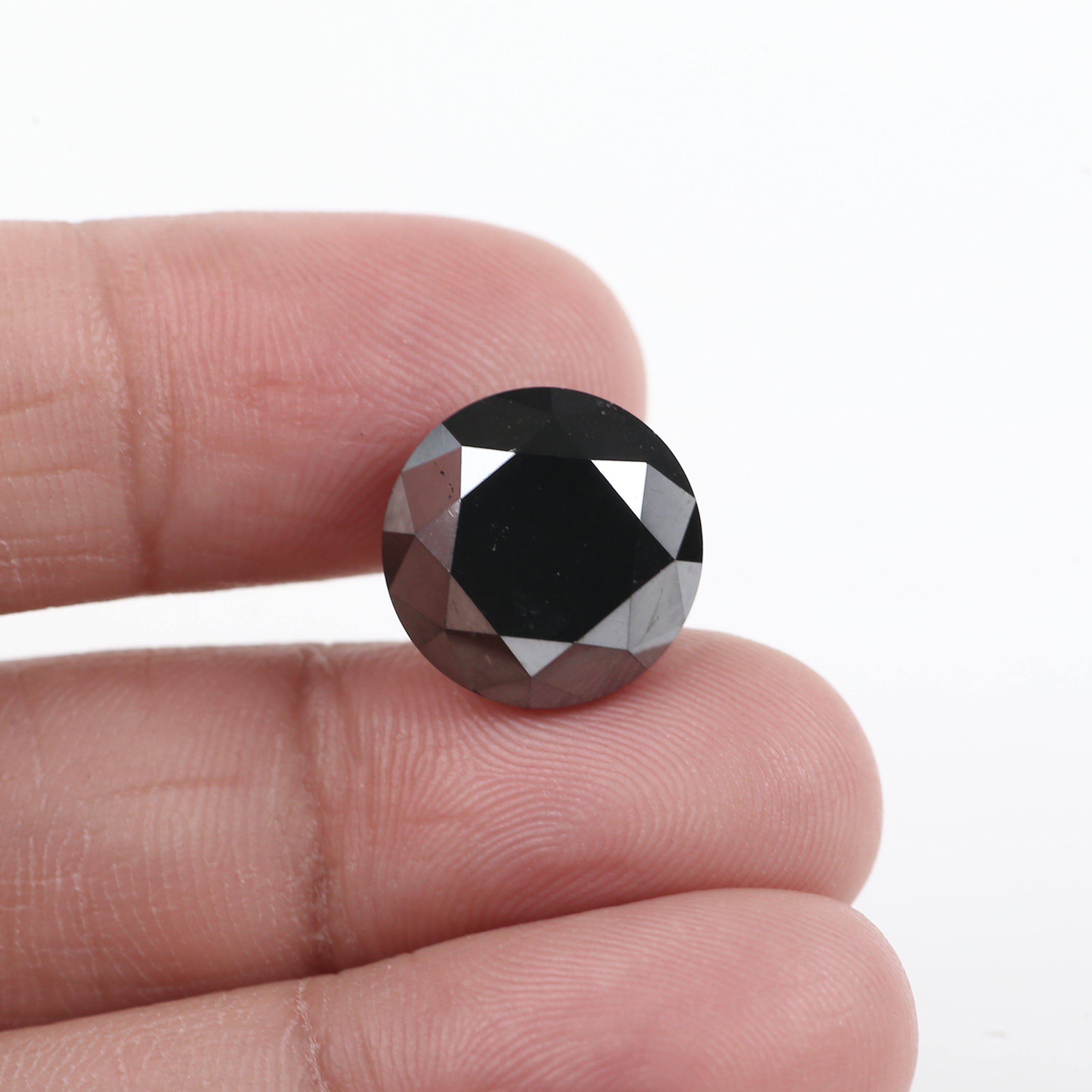 Round black diamond held between fingers against a white background