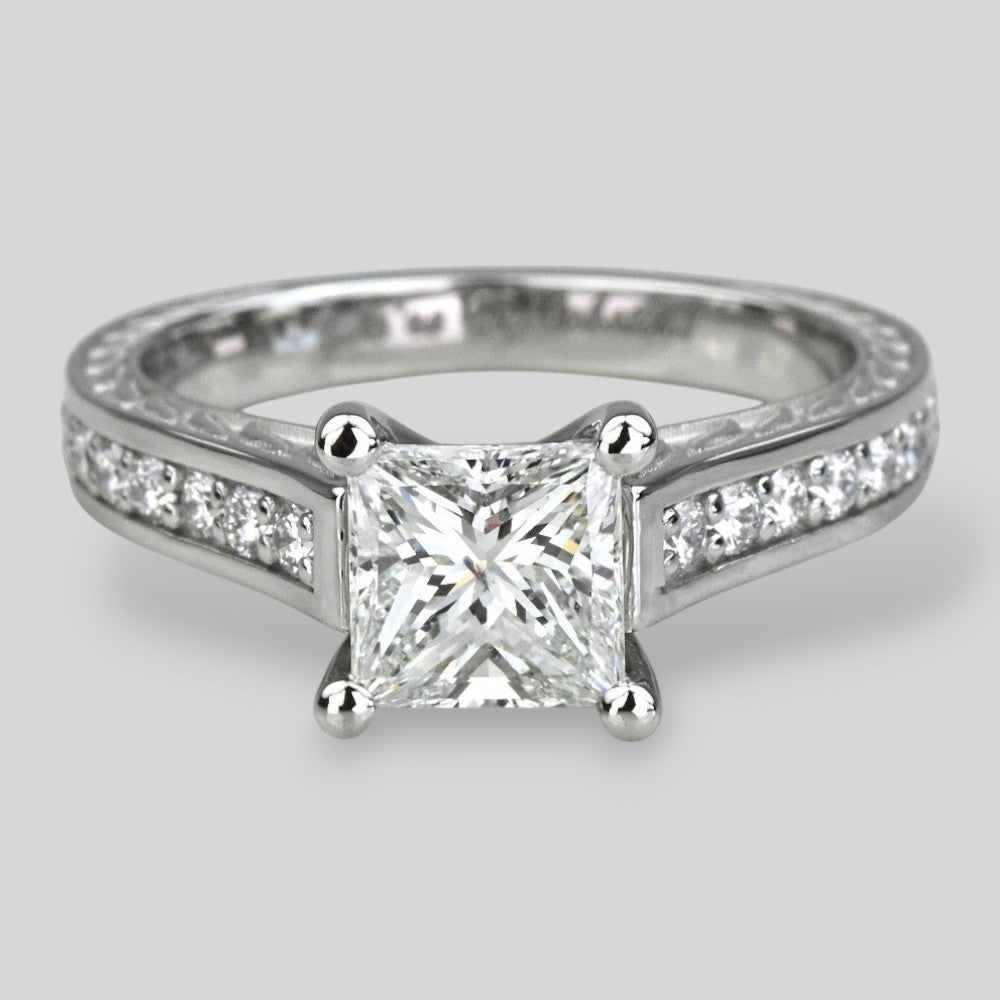 Diamond ring with a central princess-cut diamond and smaller diamonds on the band against a light gray background