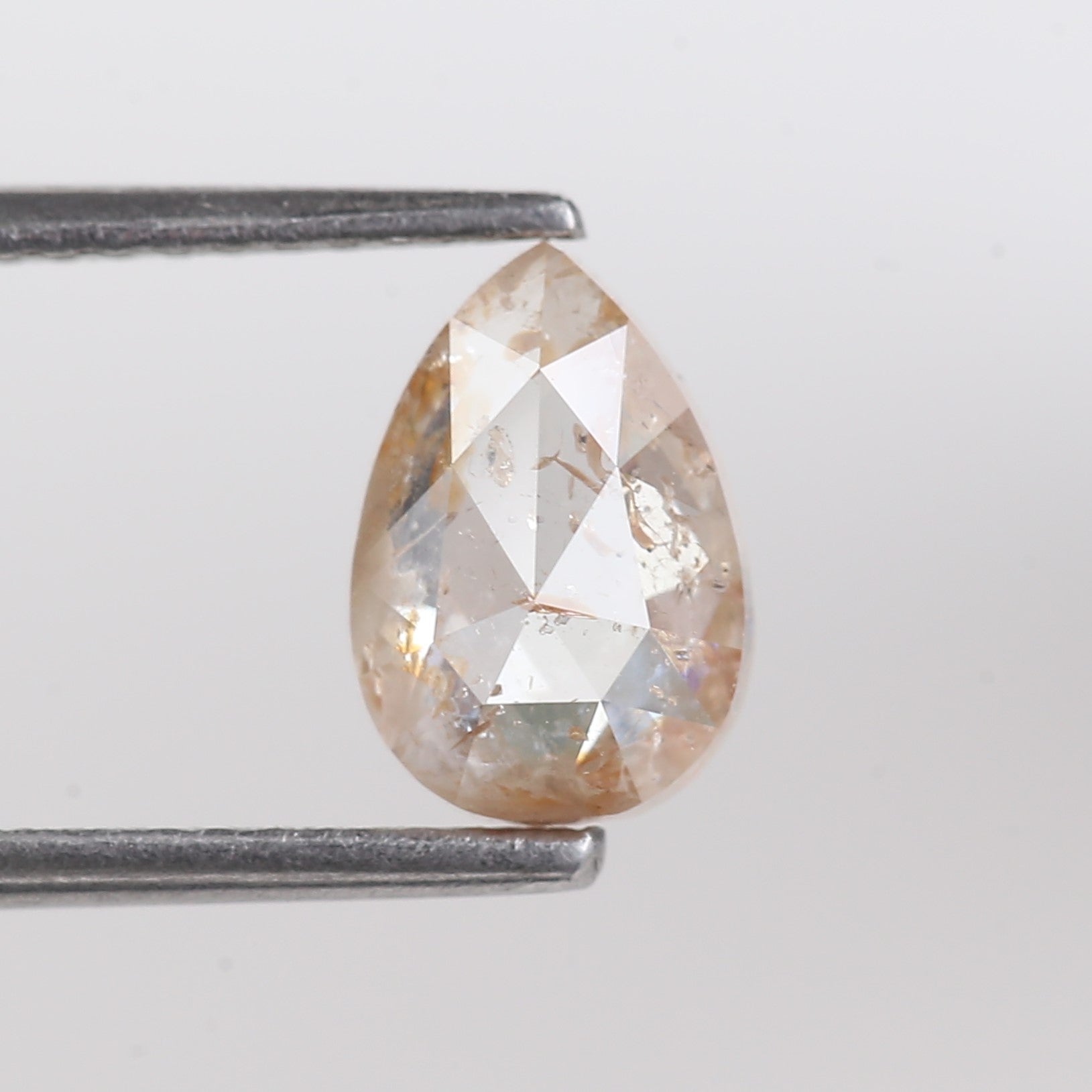 Pear-shaped diamond held between two tweezers on a light gray background