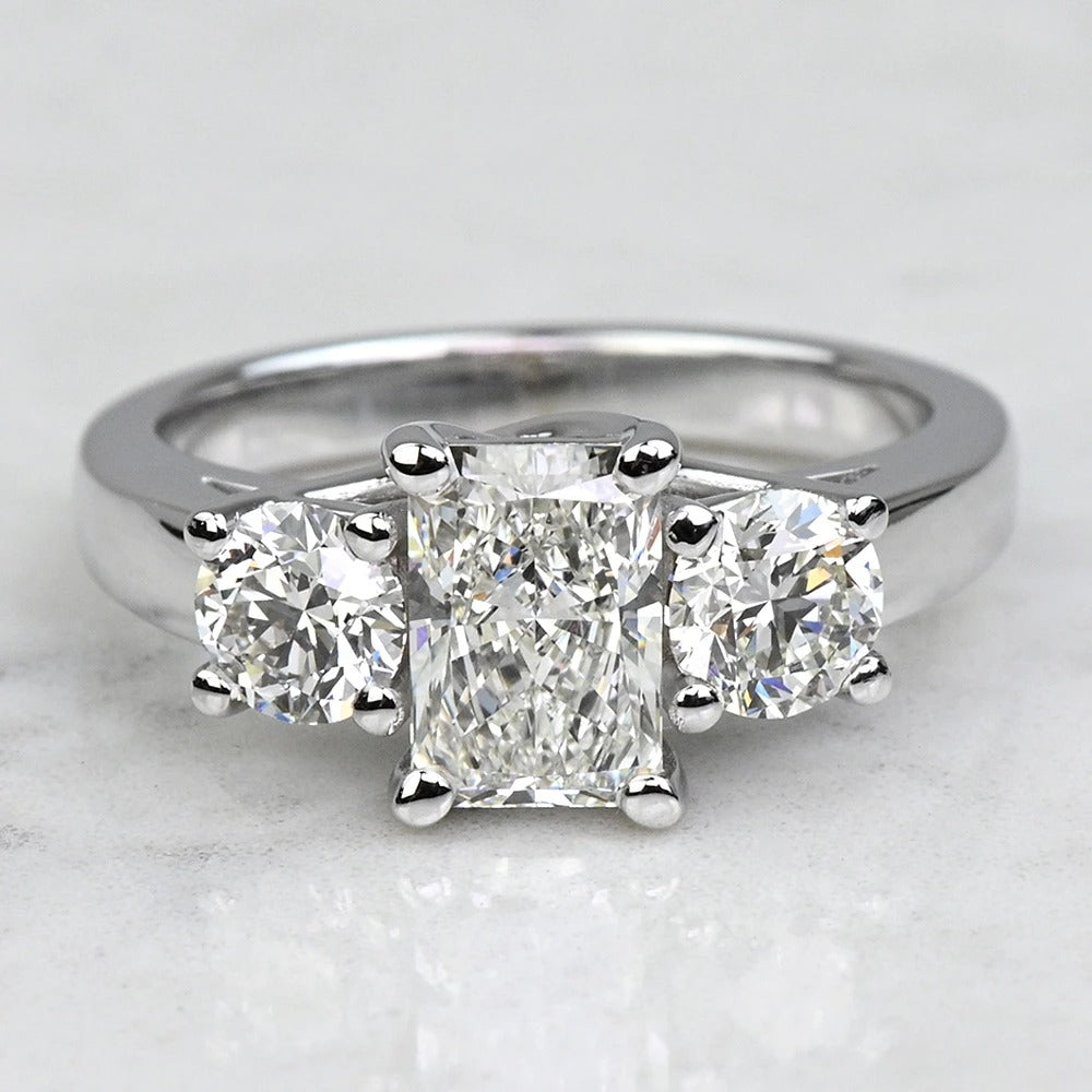 Diamond ring with three clear gemstones on a light gray background