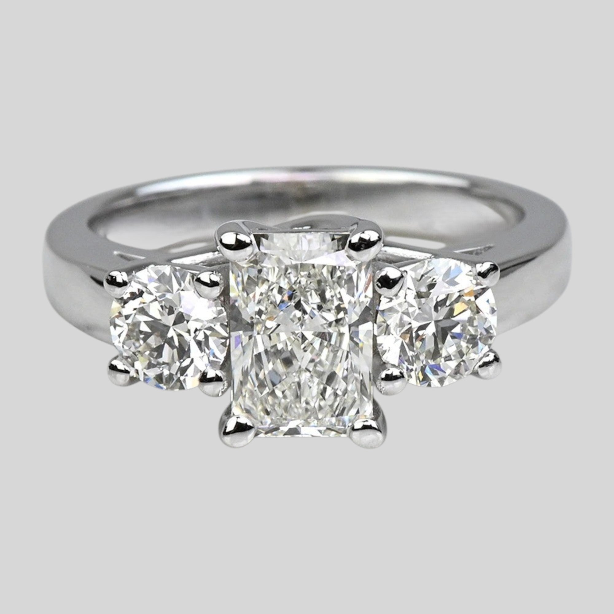 Diamond ring with three clear gemstones on a light gray background