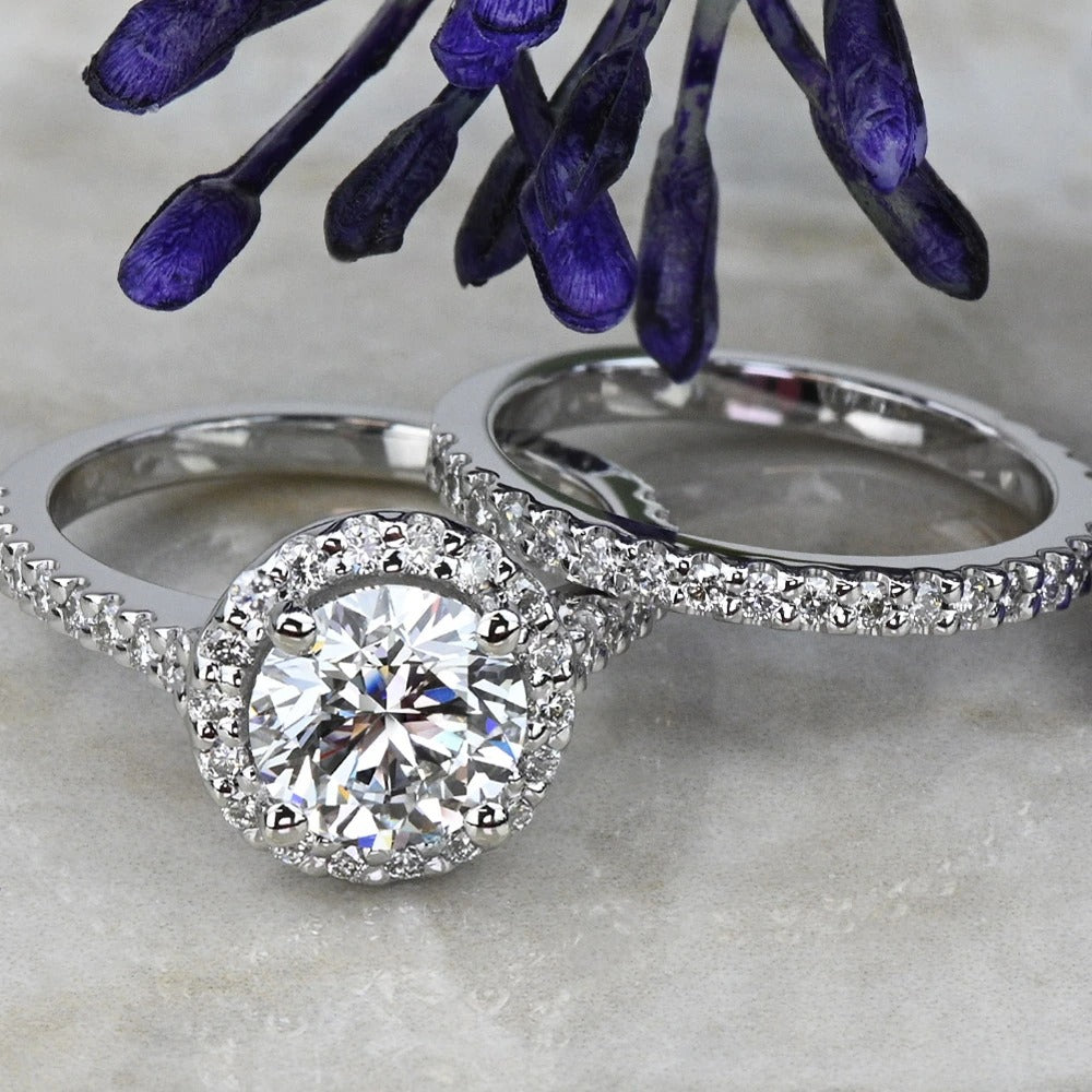 Two white gold rings with diamond accents on a textured surface with purple flowers in the background.
