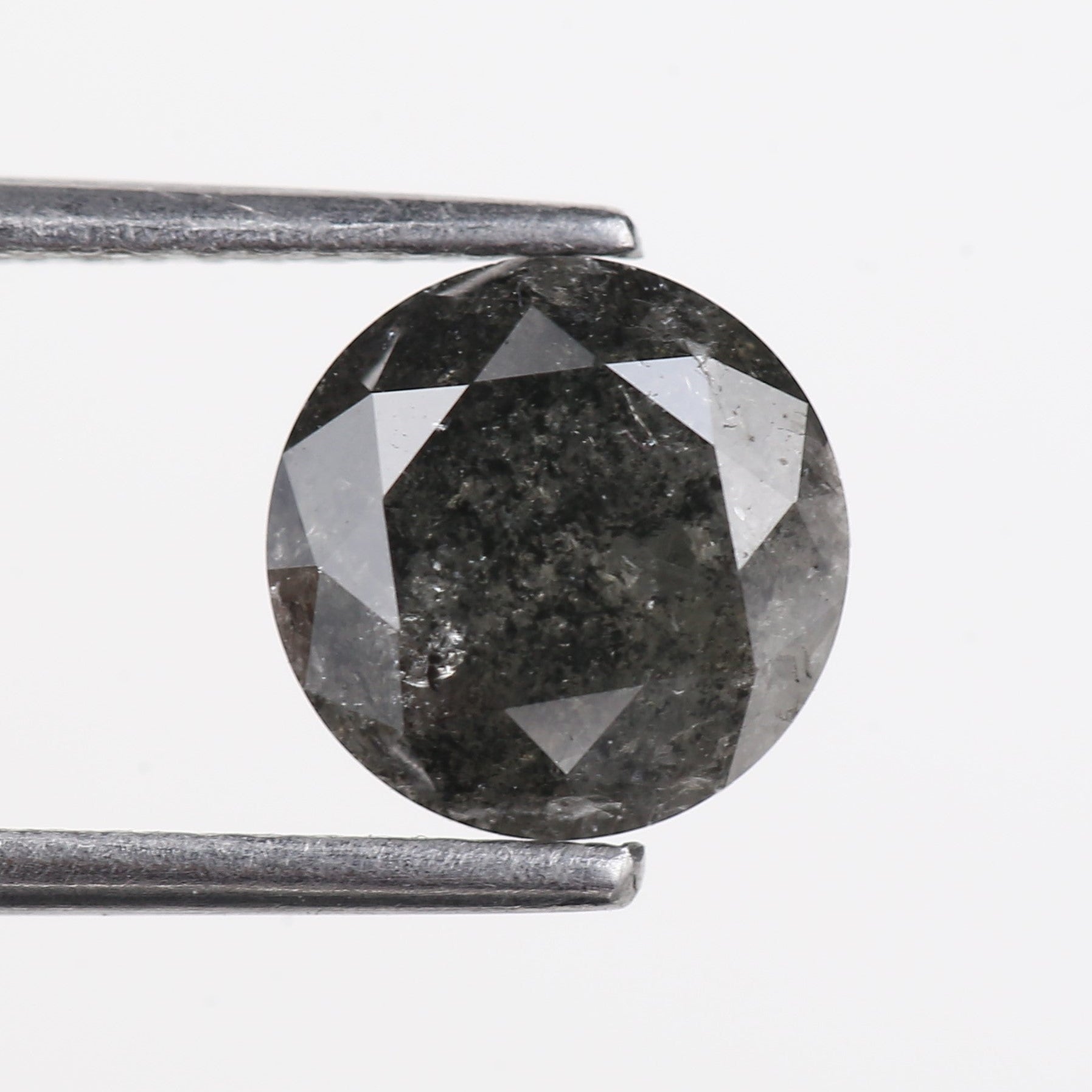 Faceted black diamond held between tweezers on a light gray background