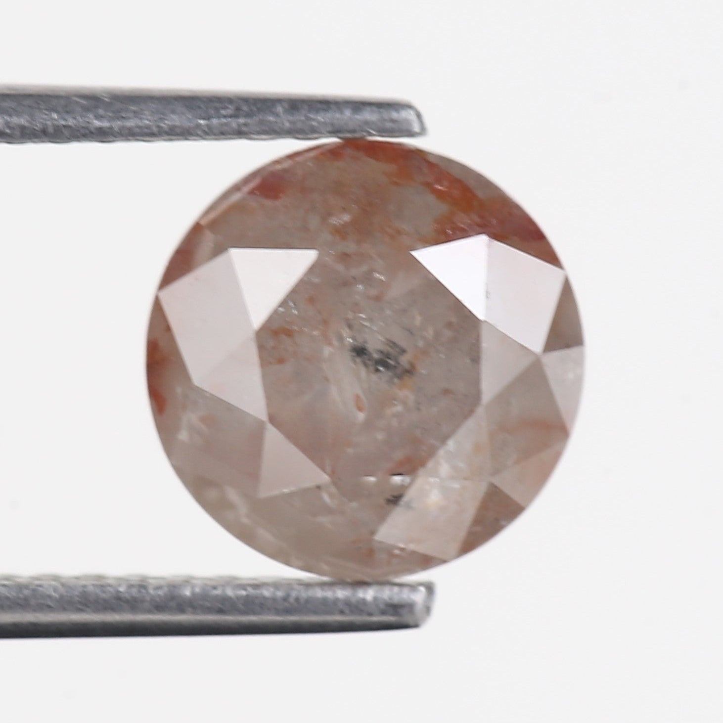 Faceted gemstone held between two metal rods on a white background