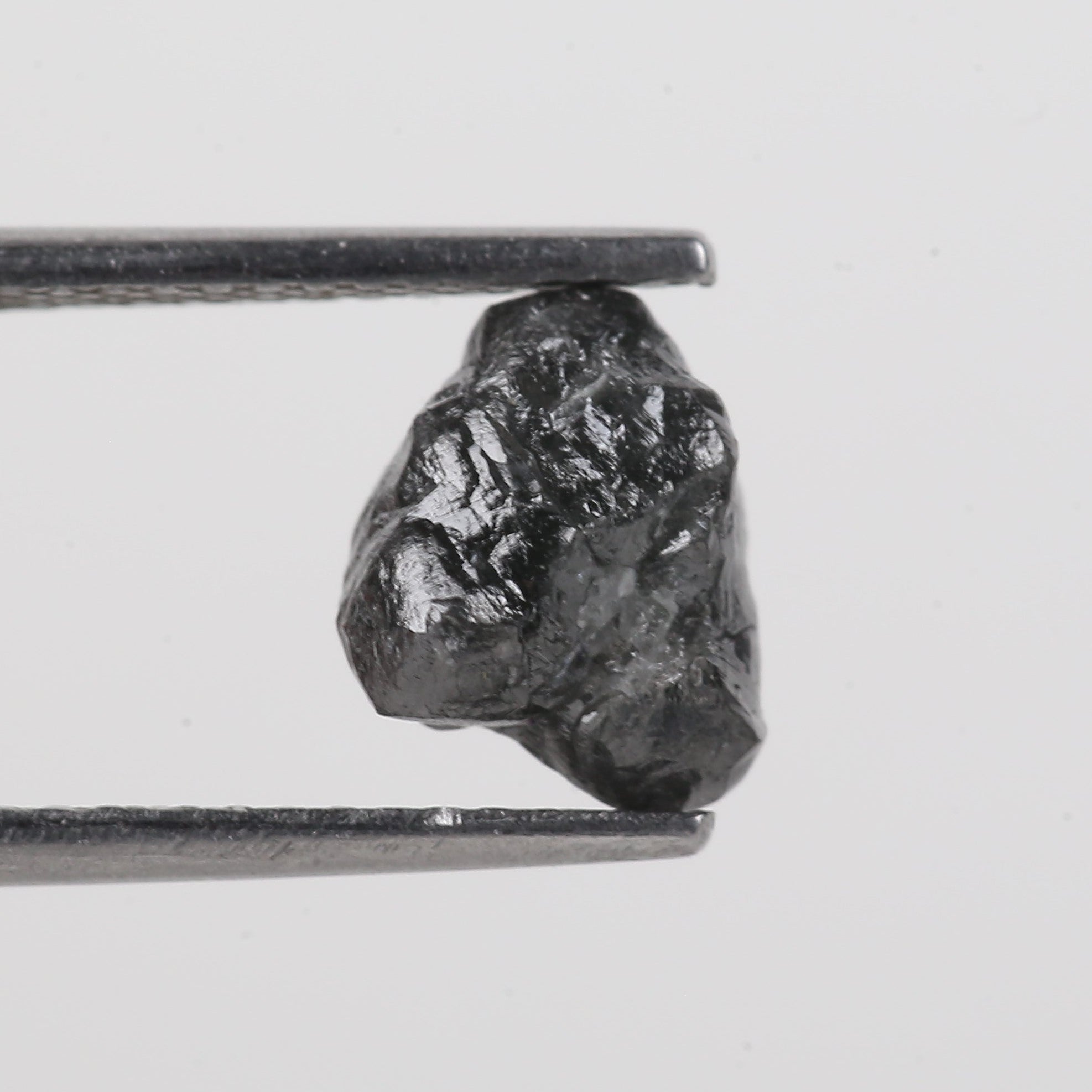 Raw diamond held between tweezers on a light gray background