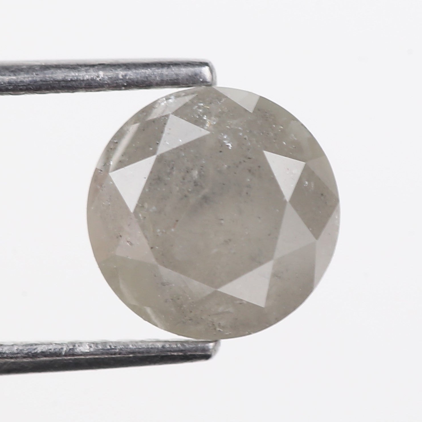 Faceted gemstone held between tweezers on a light gray background