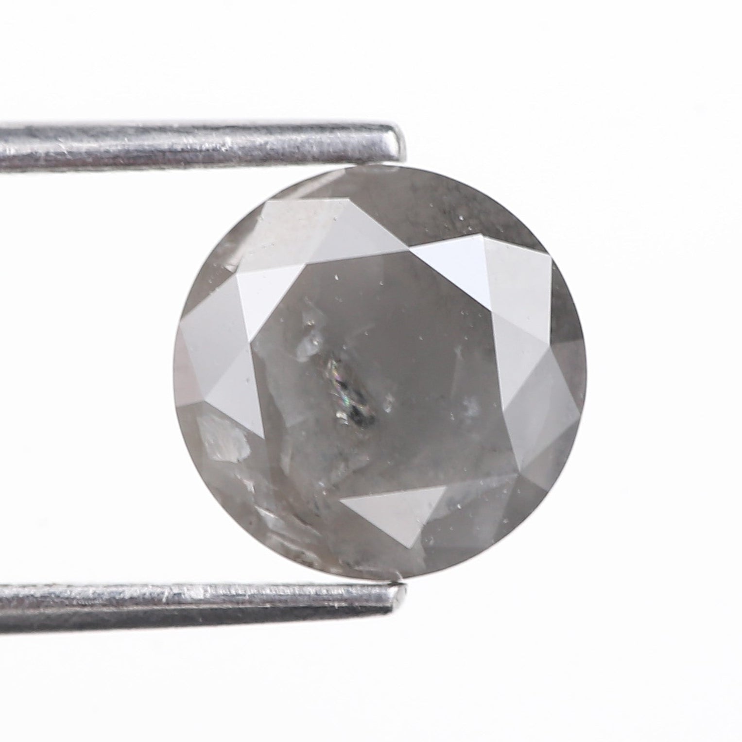 Faceted gemstone held between tweezers on a white background