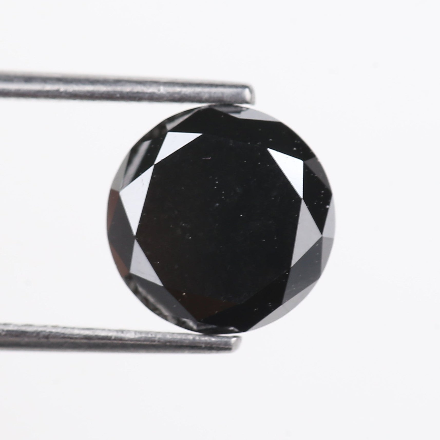 Faceted black gemstone held by tweezers on a white background
