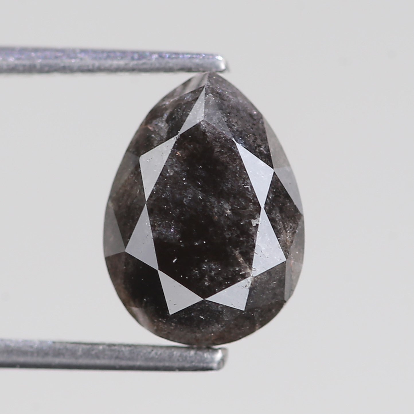 Teardrop-shaped black diamond held by tweezers on a light gray background