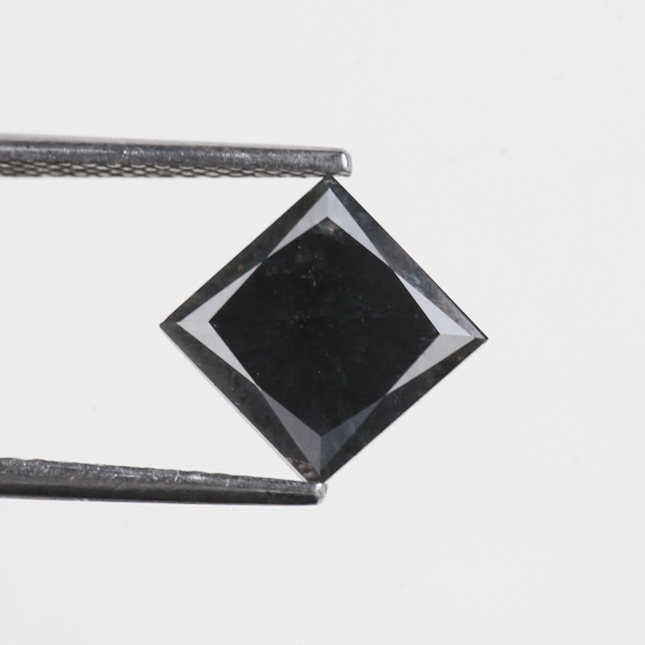 Black diamond held between tweezers on a light gray background