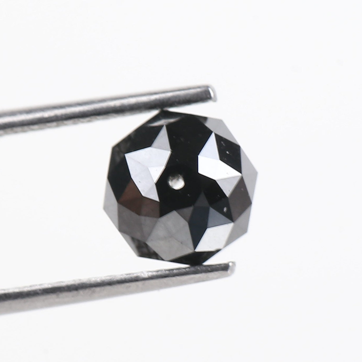 Faceted black gemstone held between tweezers on a white background