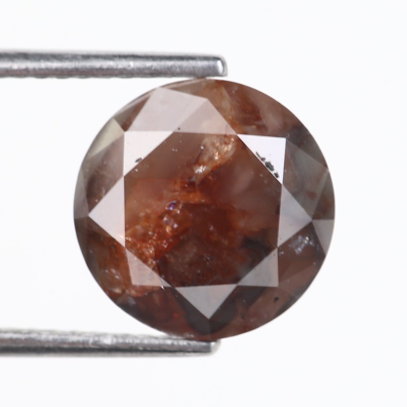 Brown diamond held between two metal prongs on a white background