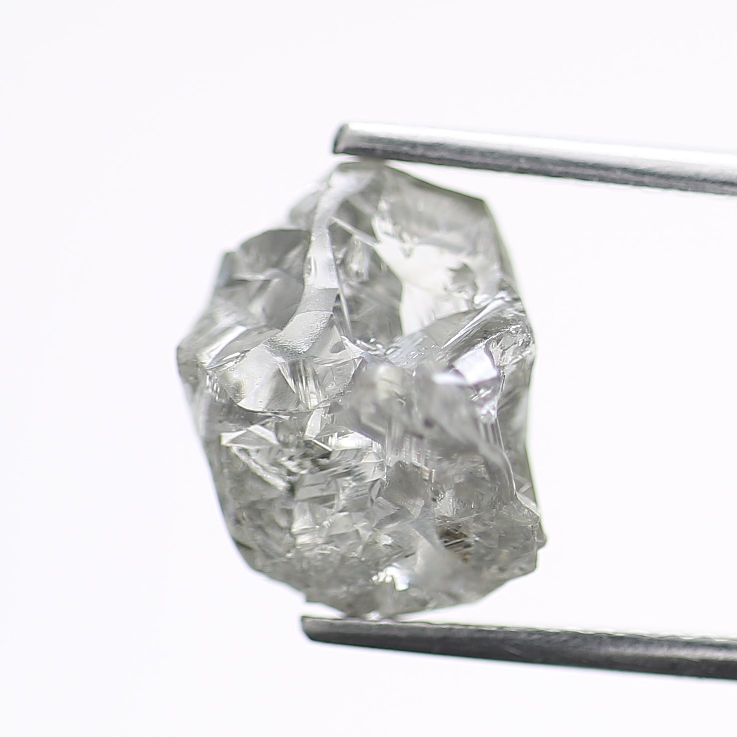 Raw diamond held by tweezers on a white background