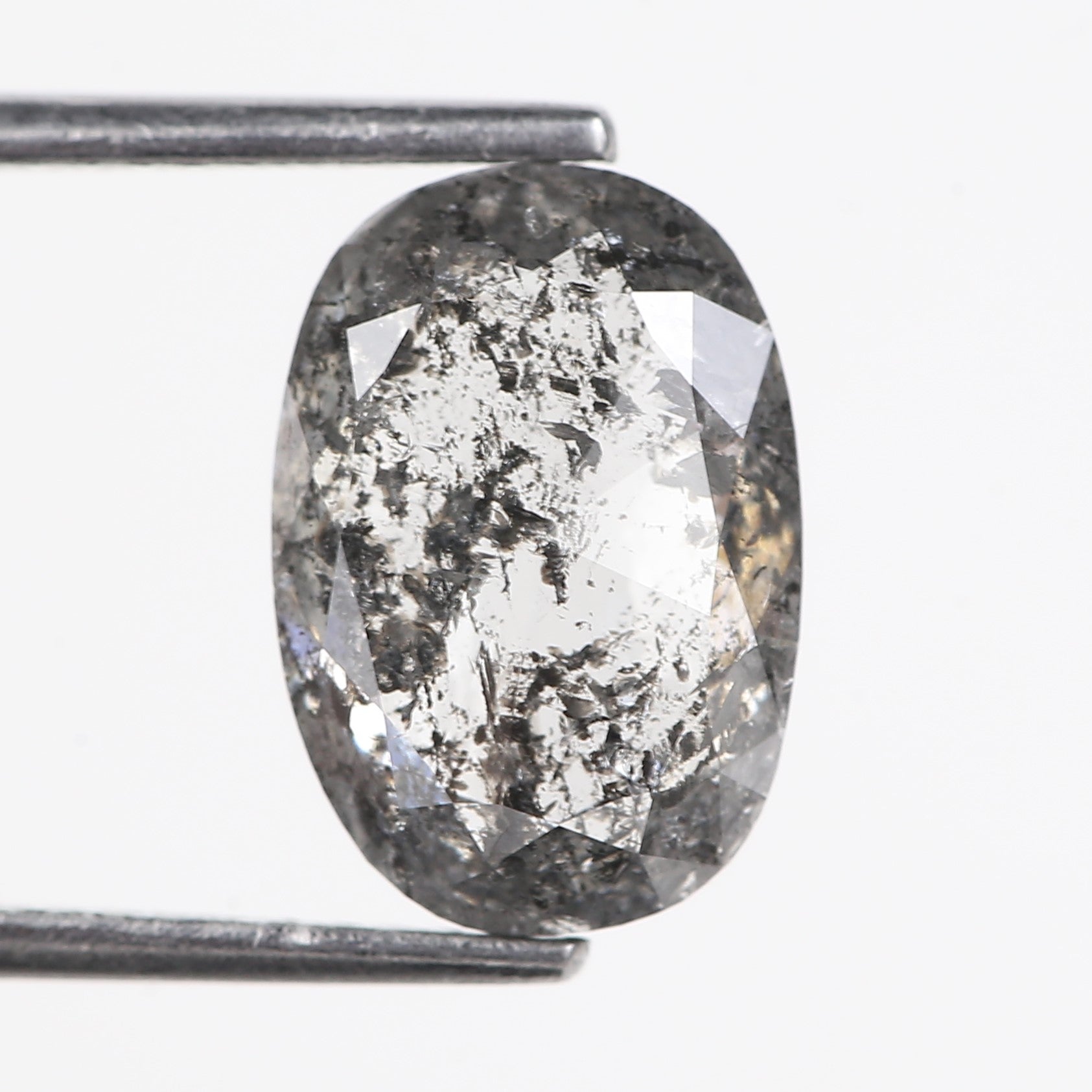 Oval-shaped diamond with gray and white speckled pattern held by tweezers on a light gray background