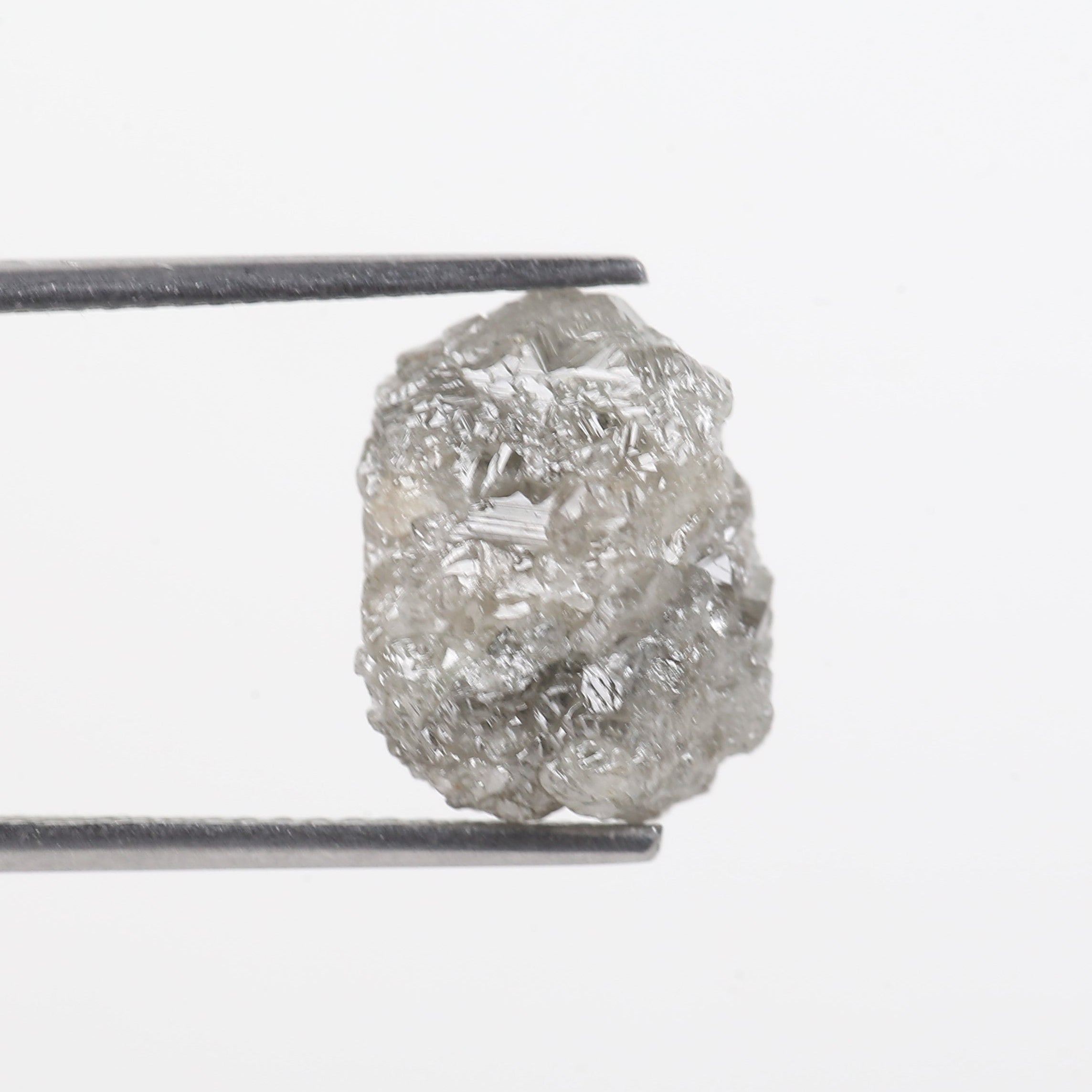 Raw diamond held by tweezers on a white background