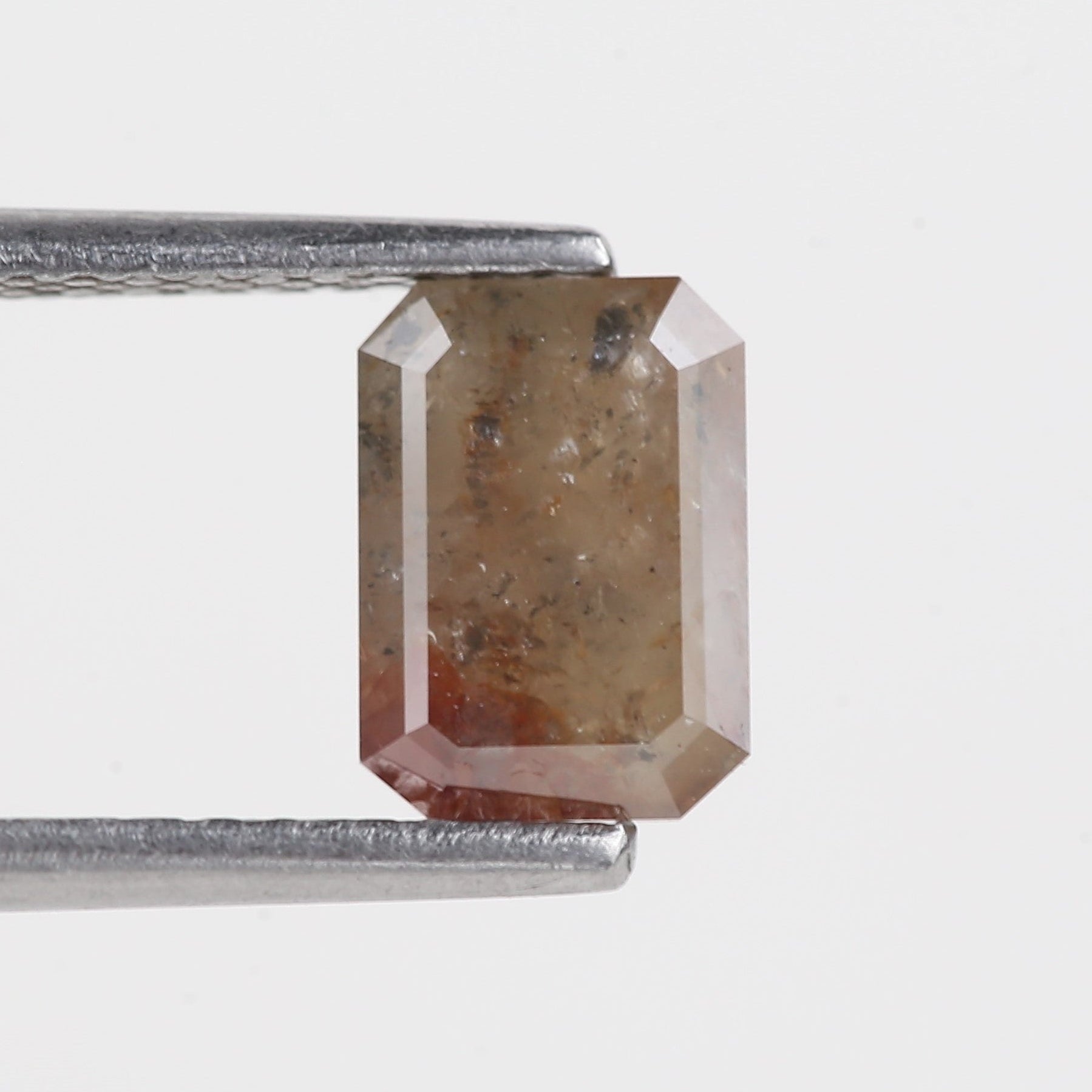 emerald brown gemstone held by tweezers on a light gray background